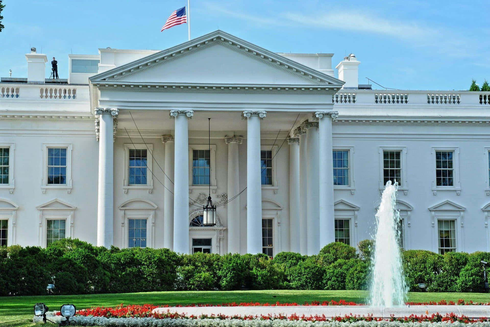 white house 桌布 壁紙 — 白宮在清澈的藍天下雄偉地矗立，前方有噴泉噴水，周圍有茂密的綠色樹籬環繞草坪。