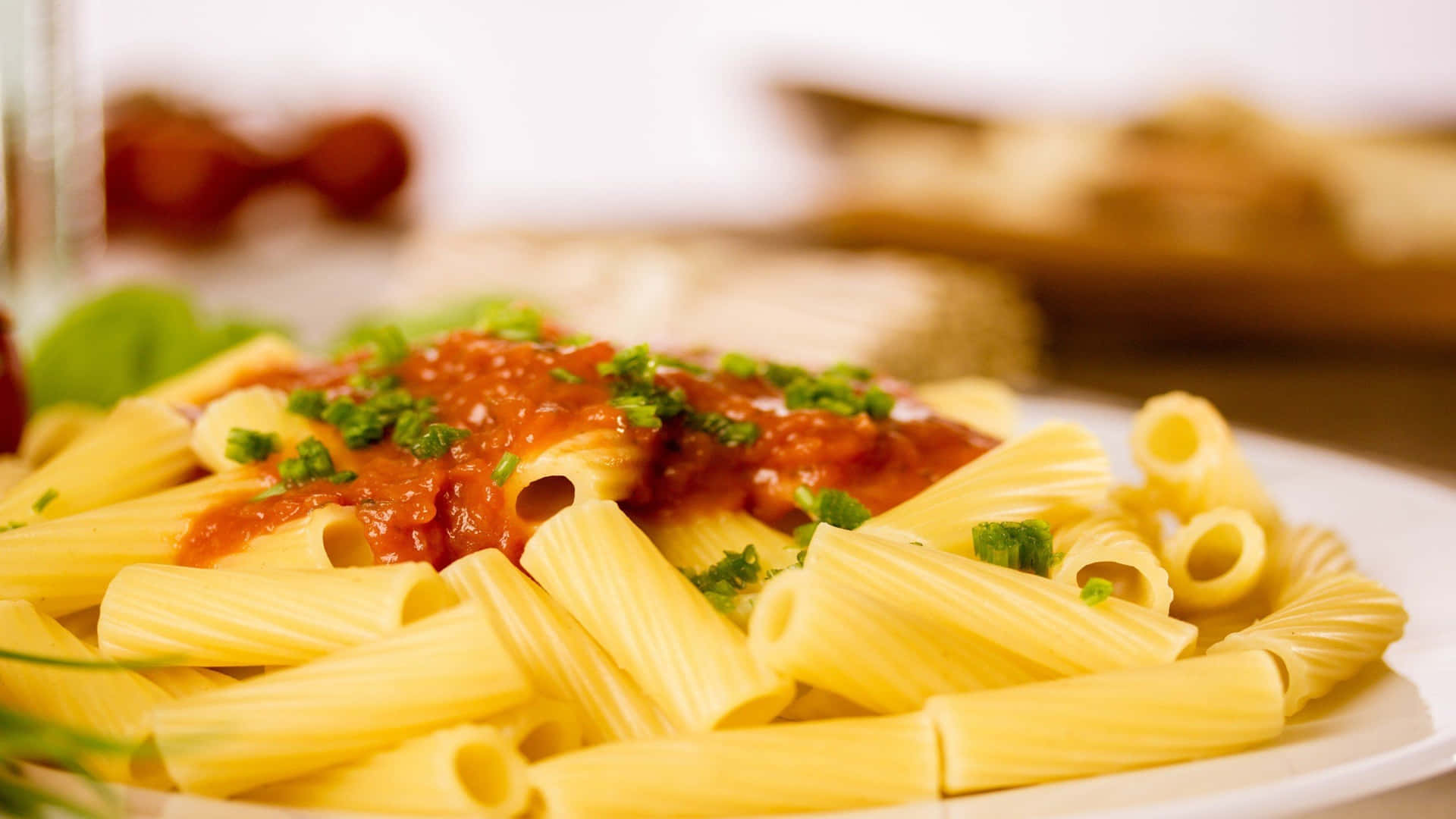 1920x1080 Pasta 桌布 壁紙 — 白盤上的rigatoni義大利麵特寫，搭配濃郁番茄醬和新鮮綠色香草。