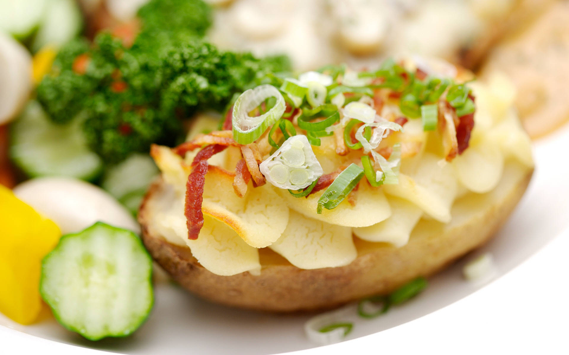 Delicious Food 桌布 壁紙 — 白盤上的烤馬鈴薯特寫，上面鋪滿脆培根和新鮮青蔥，周圍環繞著色彩繽紛的蔬菜。