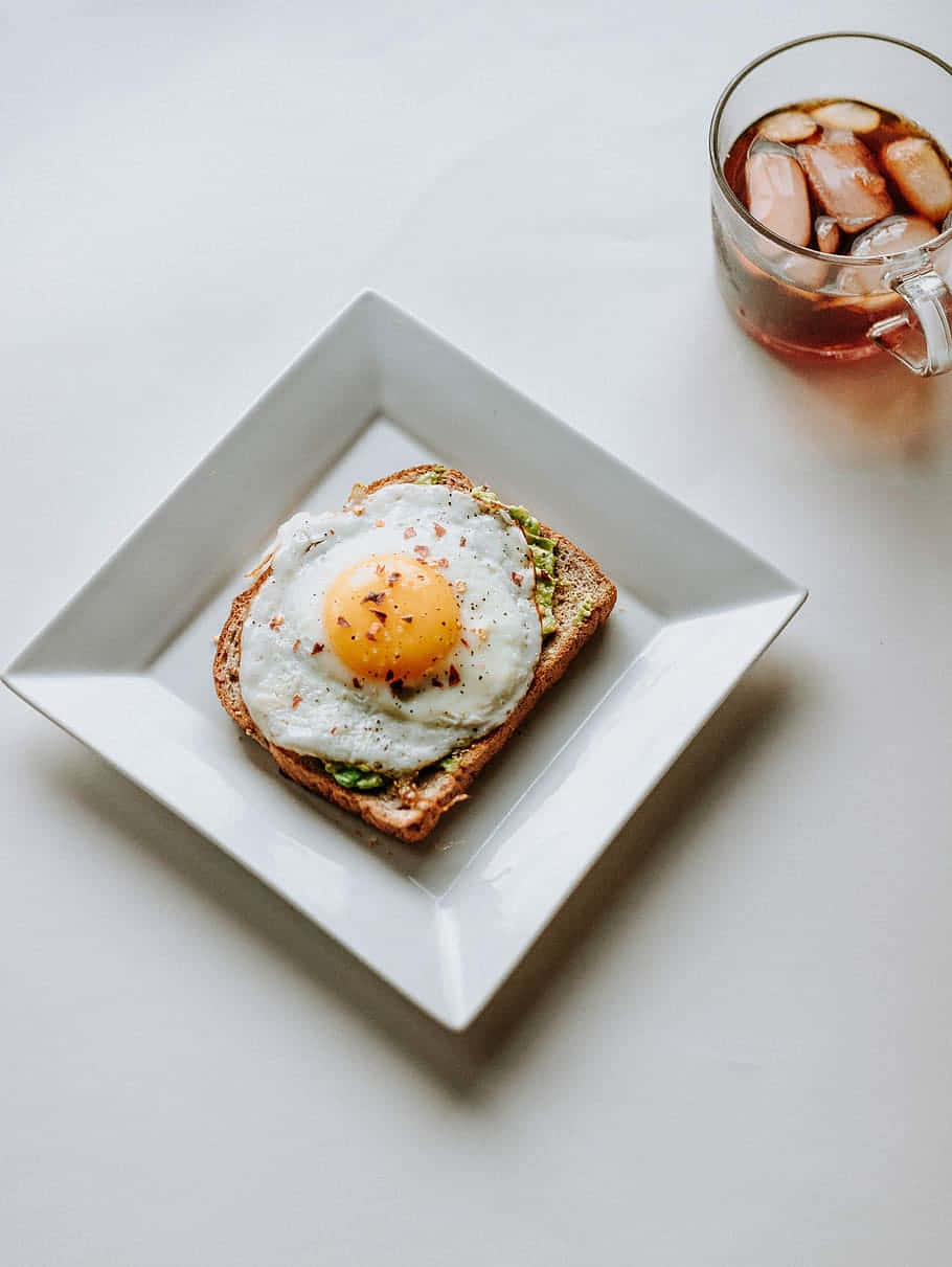 Egg White 桌布 壁紙 — 白盤上的酪梨吐司上放著太陽蛋，旁邊有一杯冰茶。