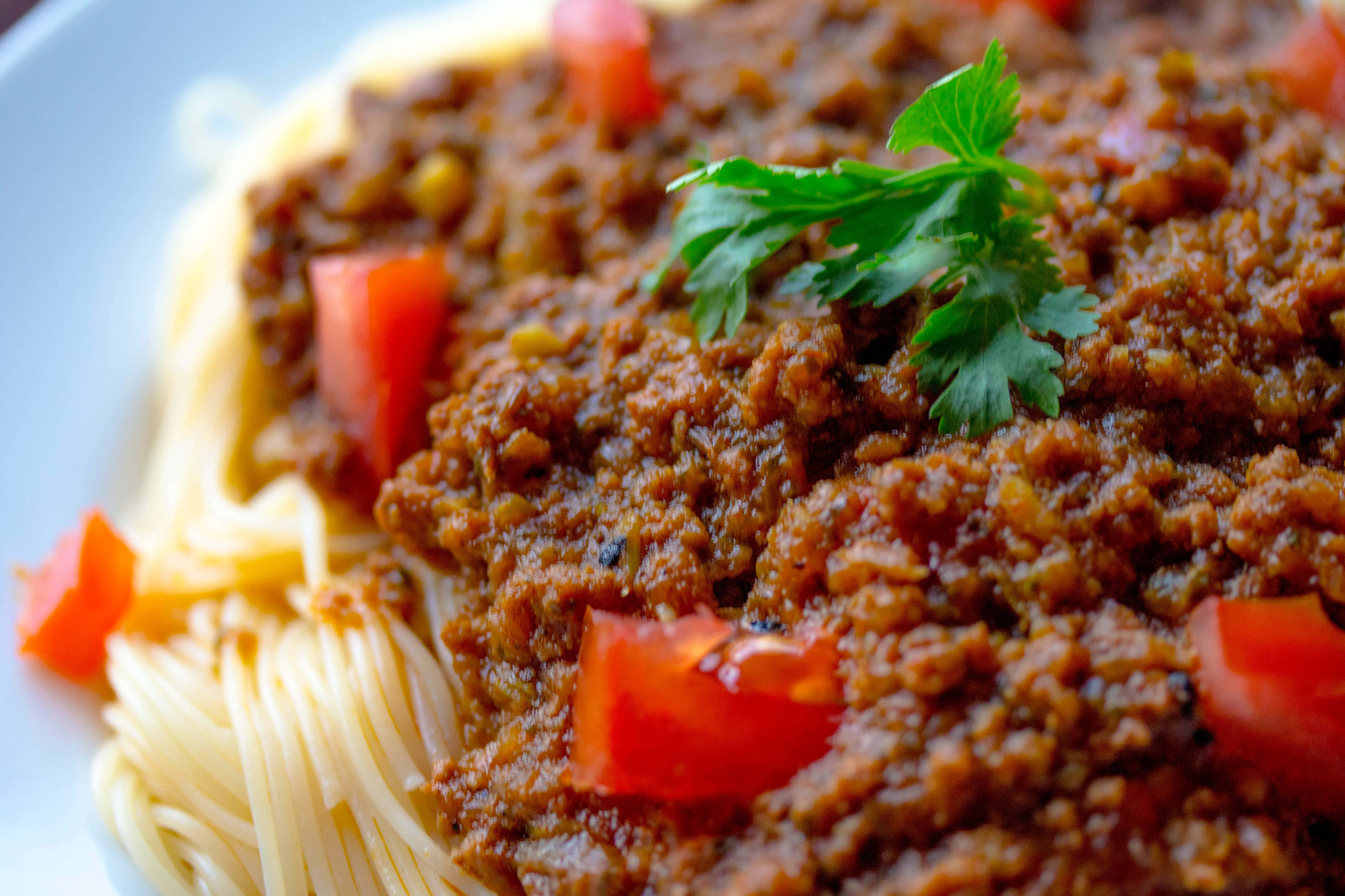 Dish 桌布 壁紙 — 白盤上義大利麵搭配濃郁肉醬、番茄丁和新鮮巴西里的特寫。