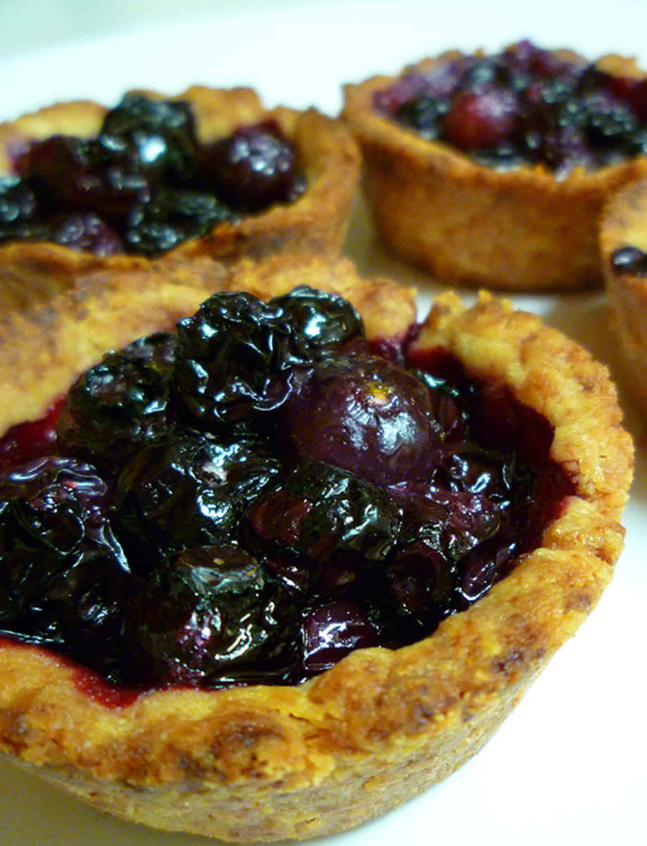 Blueberries Tart 桌布 壁紙 — 白盤上金黃酥皮藍莓塔的特寫，表面光澤亮麗。