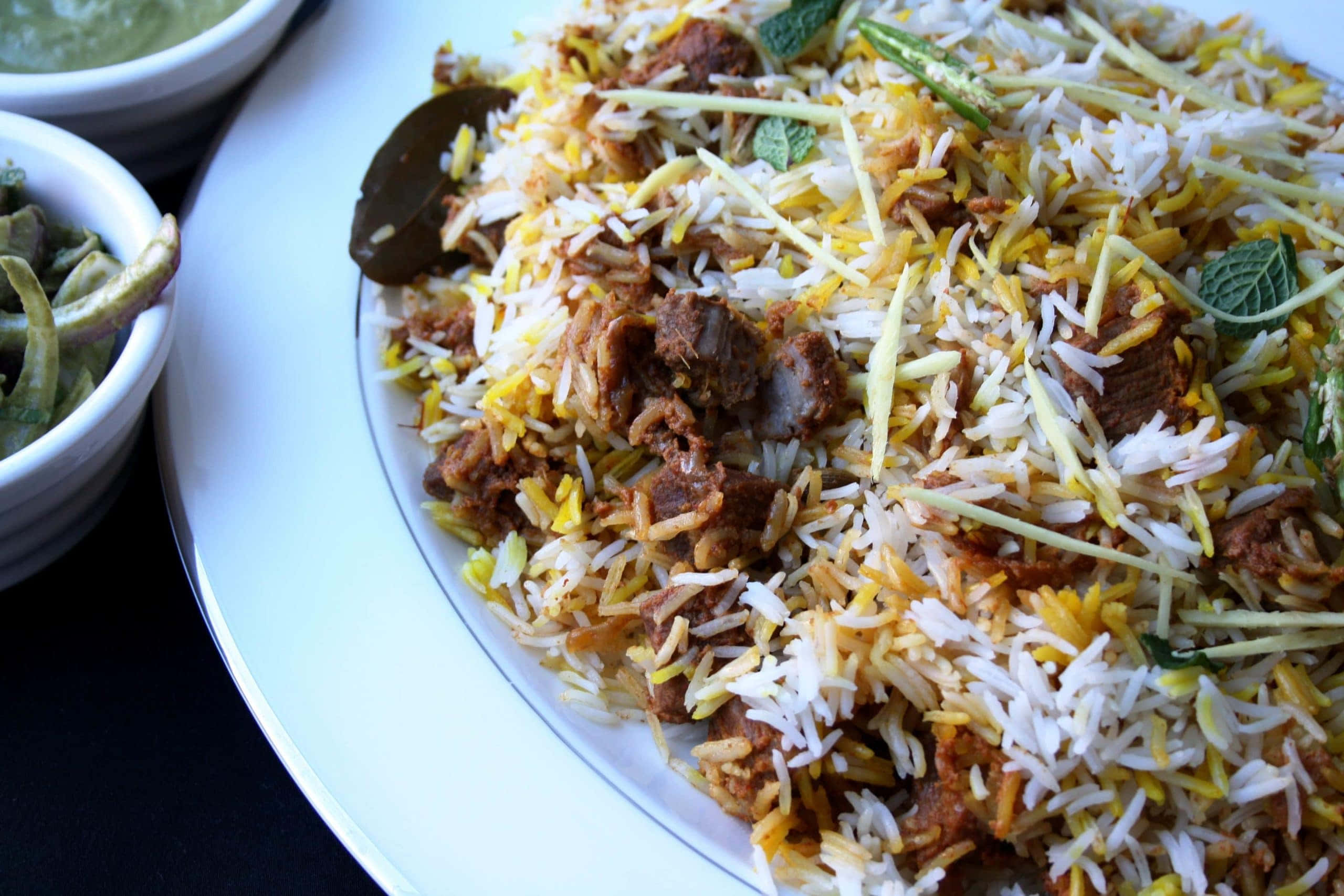 Biryani 桌布 壁紙 — 白盤上香氣撲鼻的印度香飯特寫，配有嫩肉、黃飯、薄荷和切片薑裝飾。