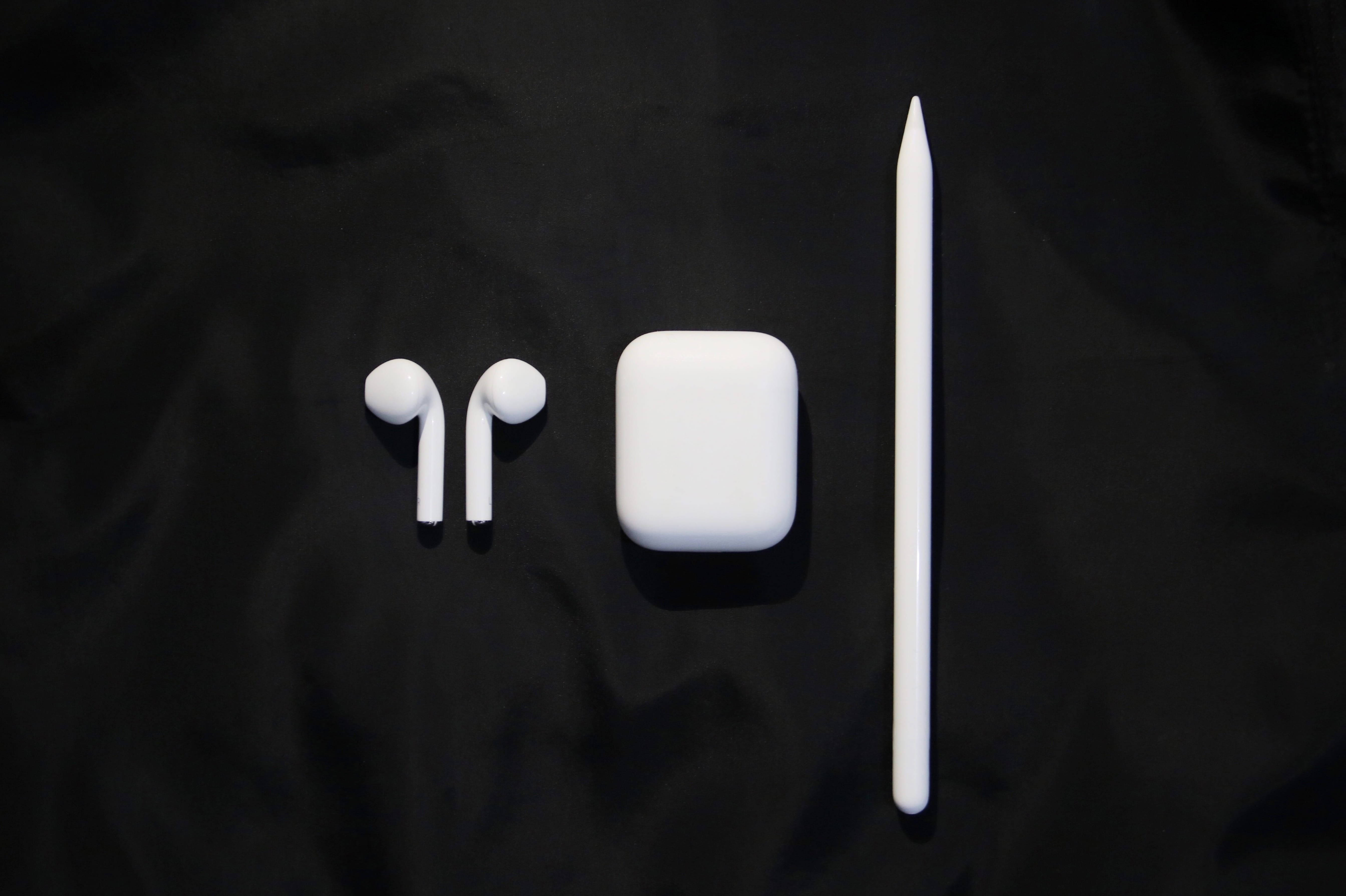 AirPods 桌布 壁紙 — 白色 Apple AirPods 保護殼、耳機和觸控筆整齊地排列在帶有紋理的黑色布料背景上。