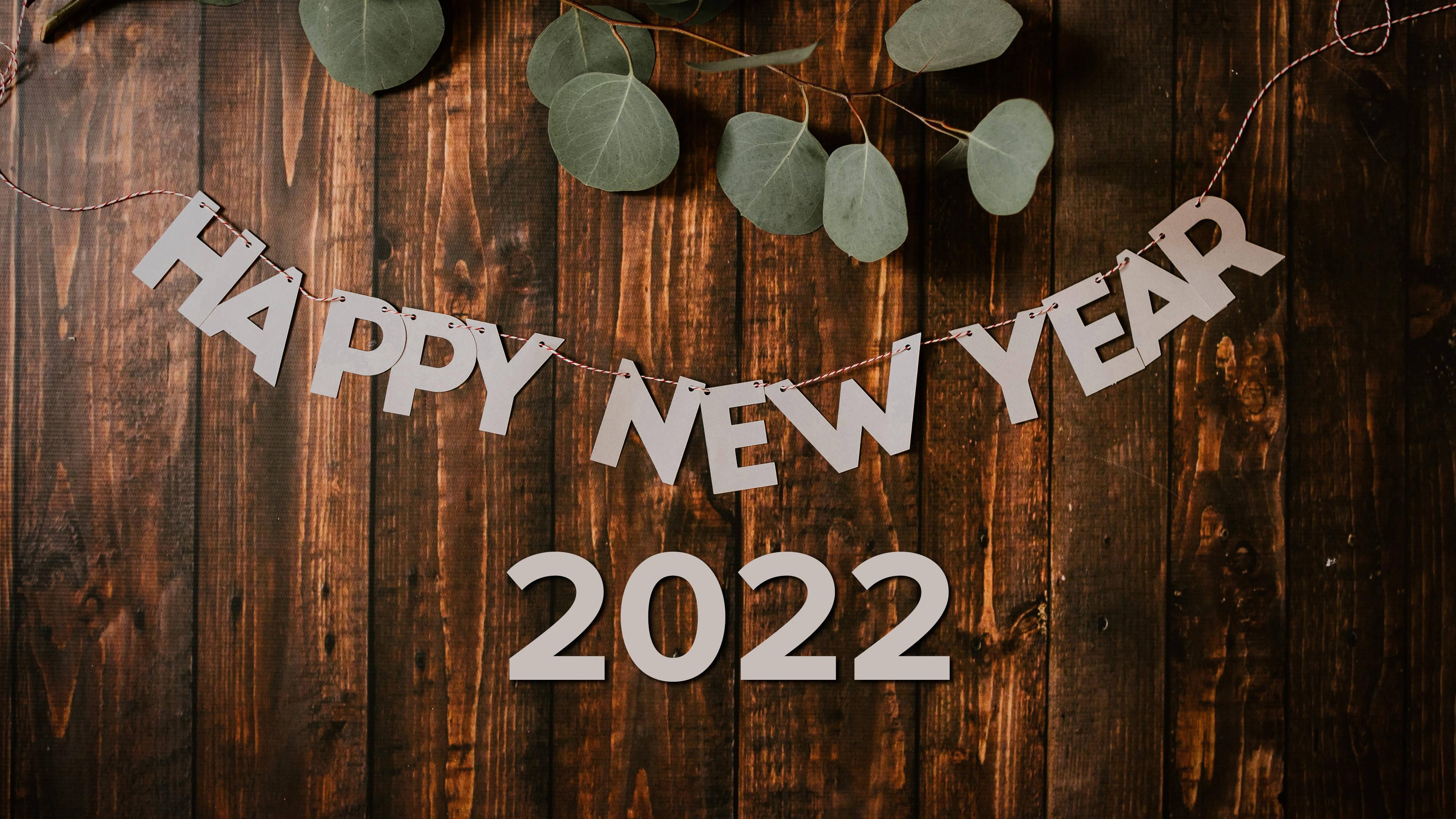 Happy New Year 2022 桌布 壁紙 — 白色 'HAPPY NEW YEAR 2022' 字母掛在裝飾著尤加利葉的鄉村風格木牆上。