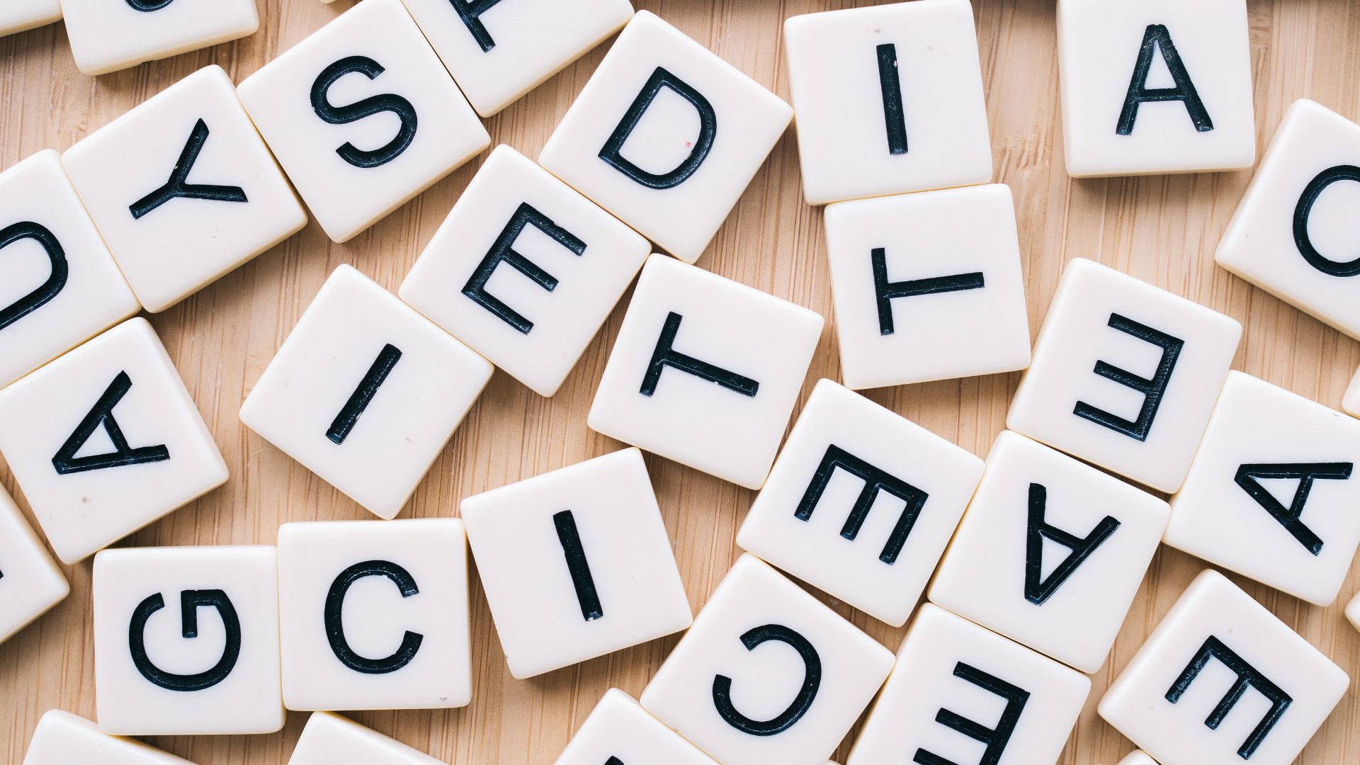 木紋 桌布 壁紙 — 白色 Scrabble 字母磚，黑色字母散落在淺色木質表面上。