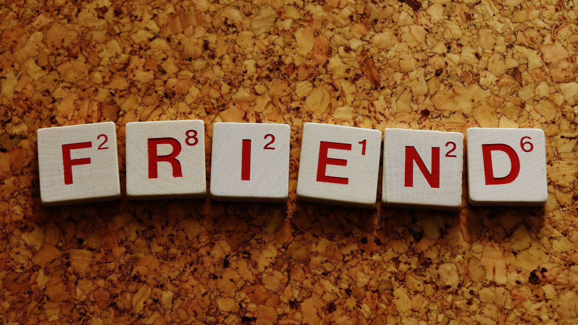 老友記 桌布 壁紙 — 白色 Scrabble 字母磚以紅色字母拼出 FRIEND，放置在帶有紋理的軟木背景上。