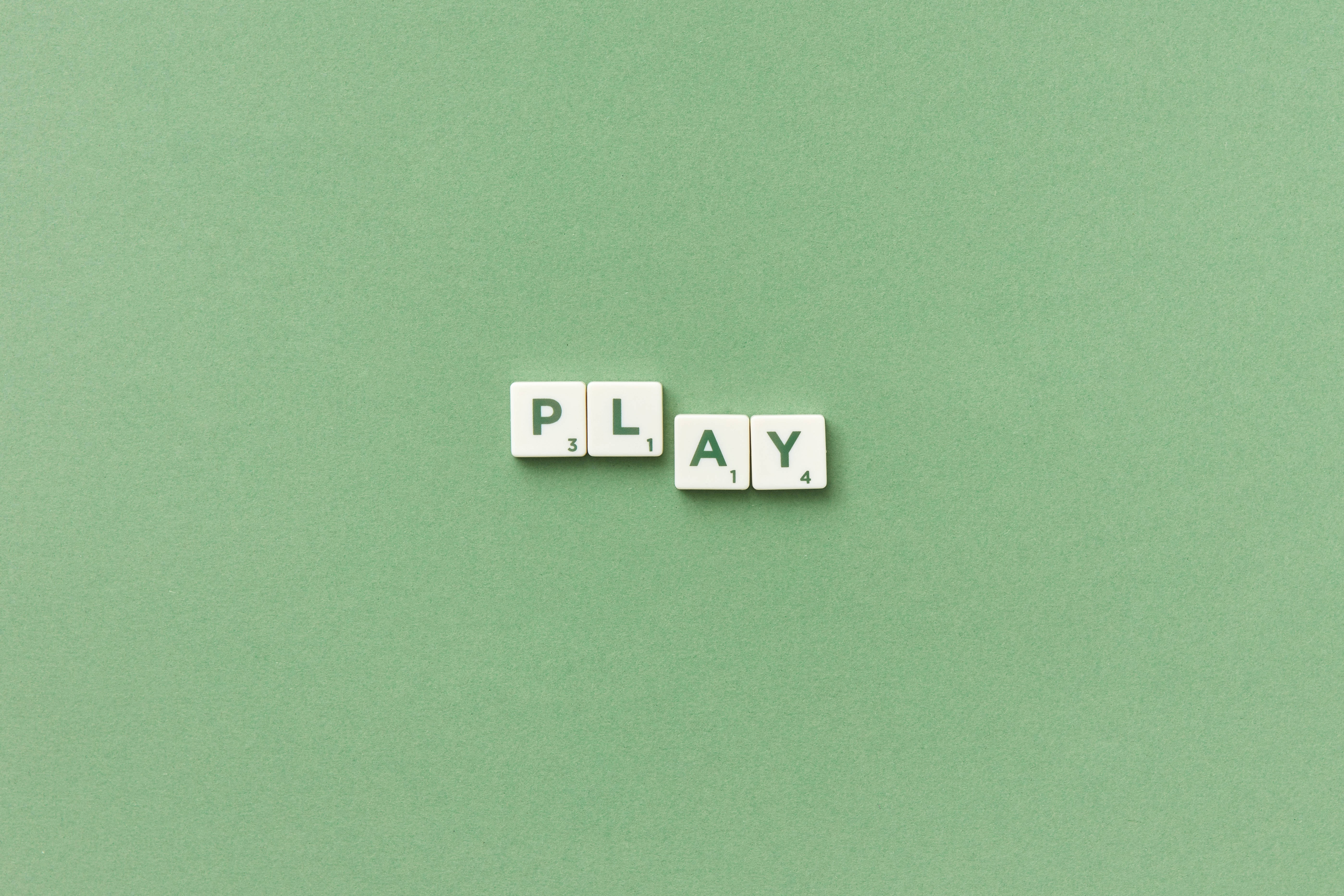 可愛粉彩風格 桌布 壁紙 — 白色 Scrabble 字母磚拼出 play，放置在柔軟的綠色紋理表面上。