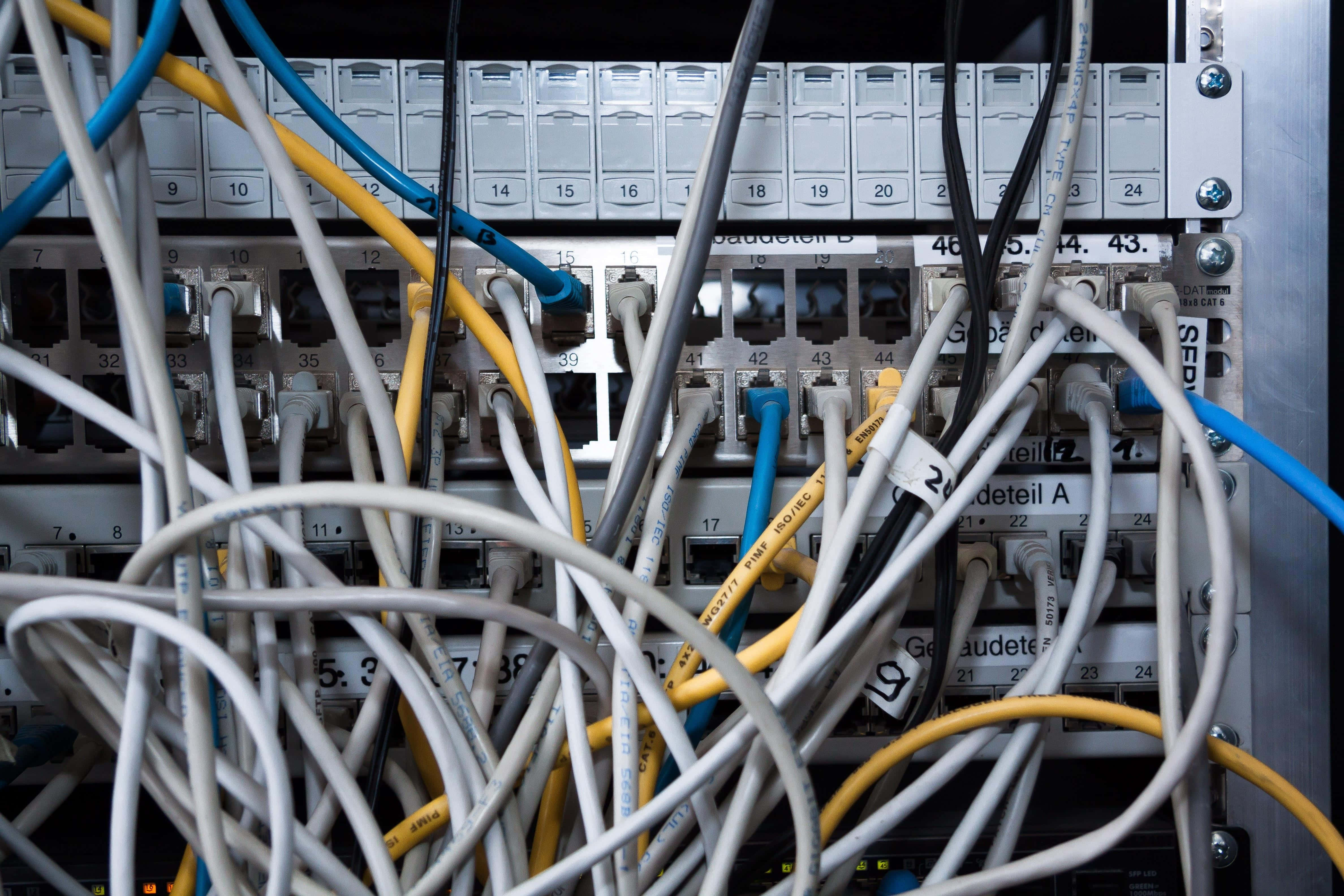 Ethernet 桌布 壁紙 — 白色、黃色和藍色網路線混亂纏結，插入伺服器機架連接埠面板。
