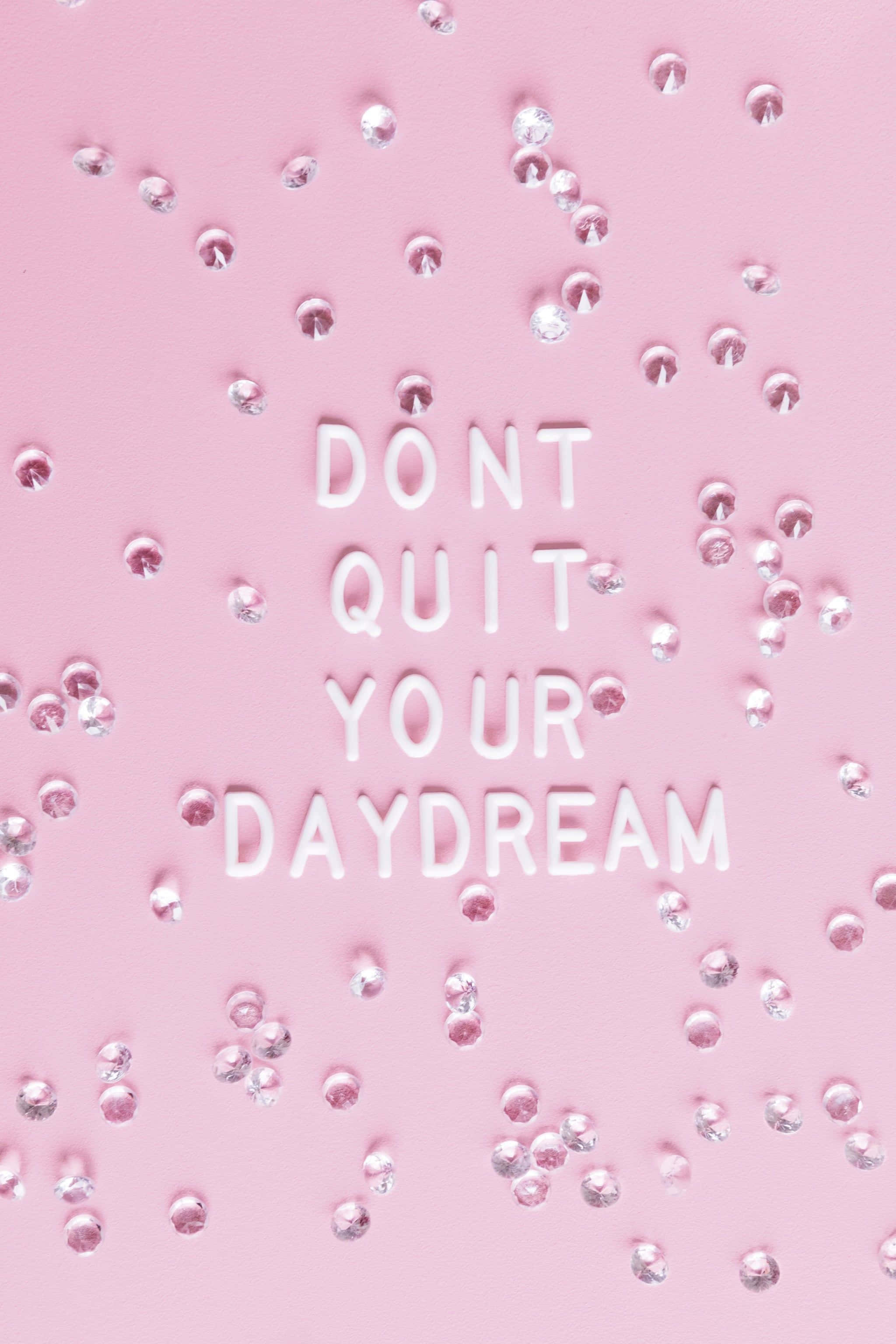 「看看你已經走了多遠。你可以的！」 壁紙 — 白色3D字母拼出「DON'T QUIT YOUR DAYDREAM」，散落在柔軟的粉紅色表面上，點綴著閃亮的銀色水鑽。