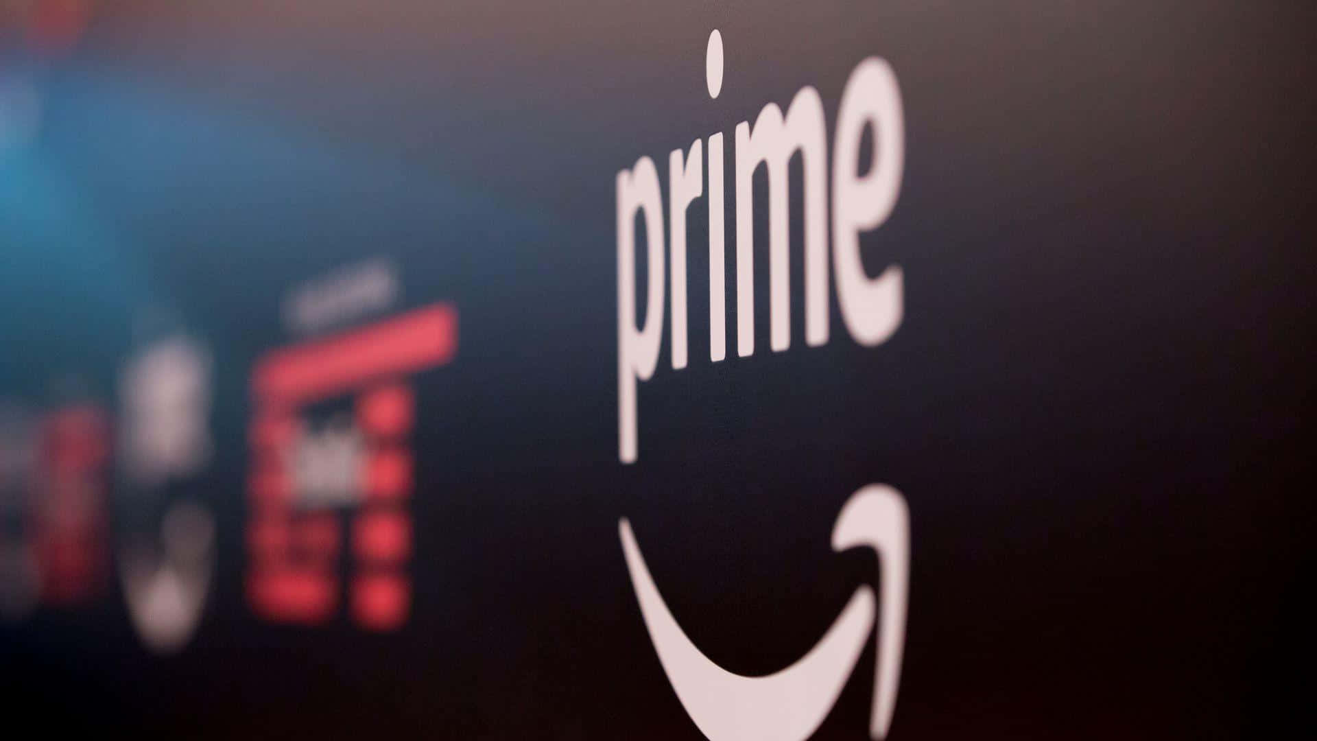 亞馬遜 桌布 壁紙 — 白色Amazon Prime標誌特寫，帶有微笑箭頭，背景為深色，遠處有模糊的彩色元素。