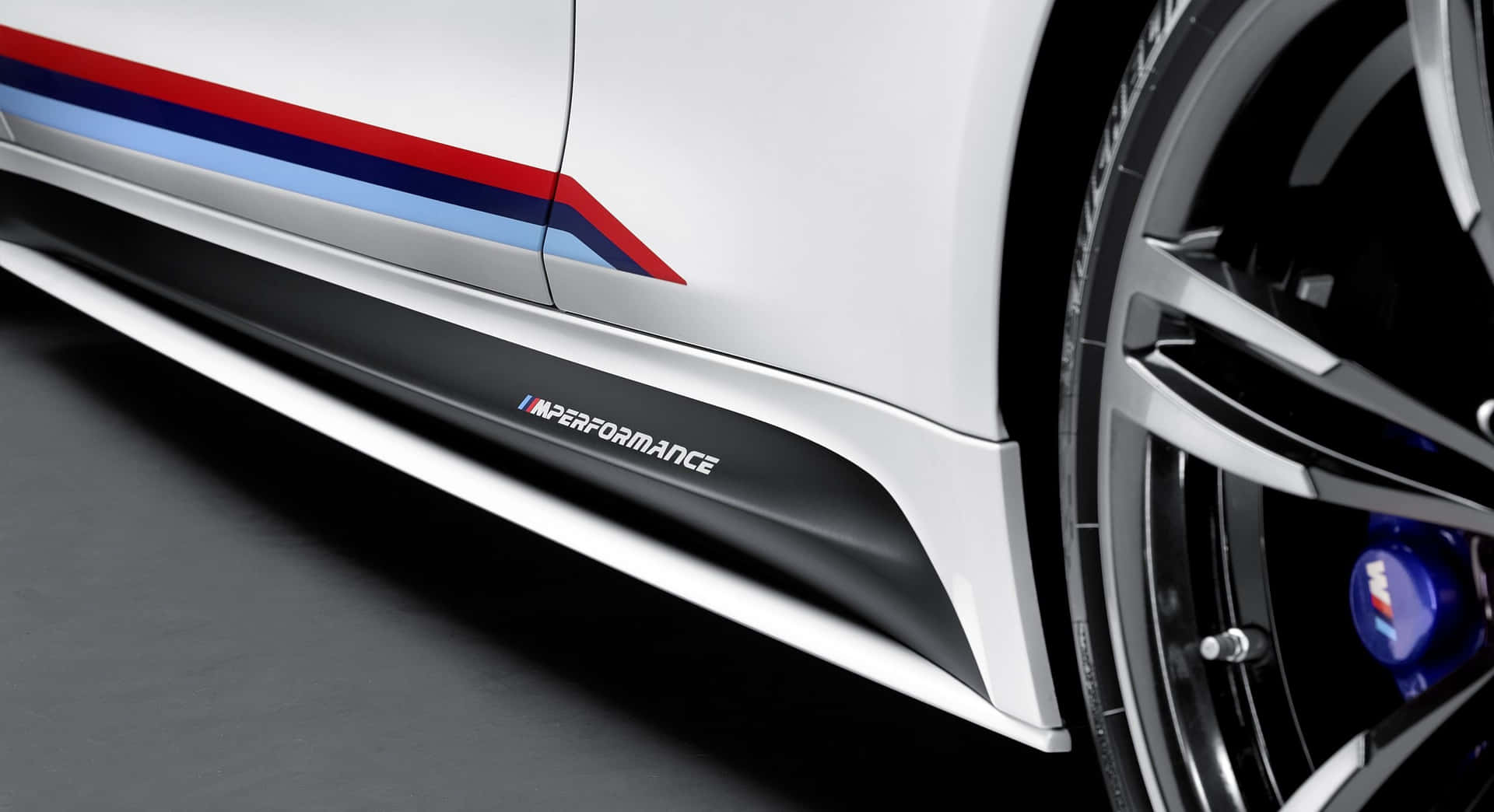 BMW 動圖 桌布 壁紙 — 白色BMW M Performance汽車特寫，展示標誌性的藍、紅、白條紋和時尚合金輪圈。