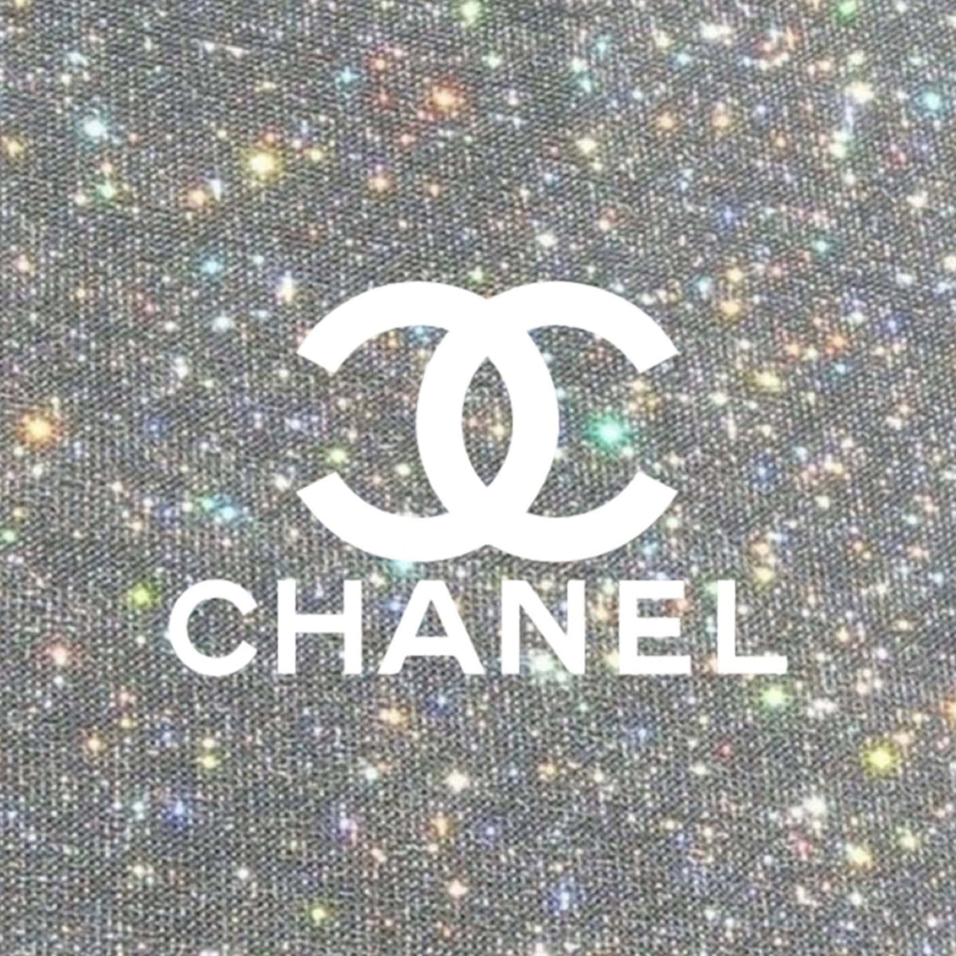 Chanel 桌布 壁紙 — 白色Chanel標誌居中於閃爍銀色布料背景上，帶有多彩閃光。