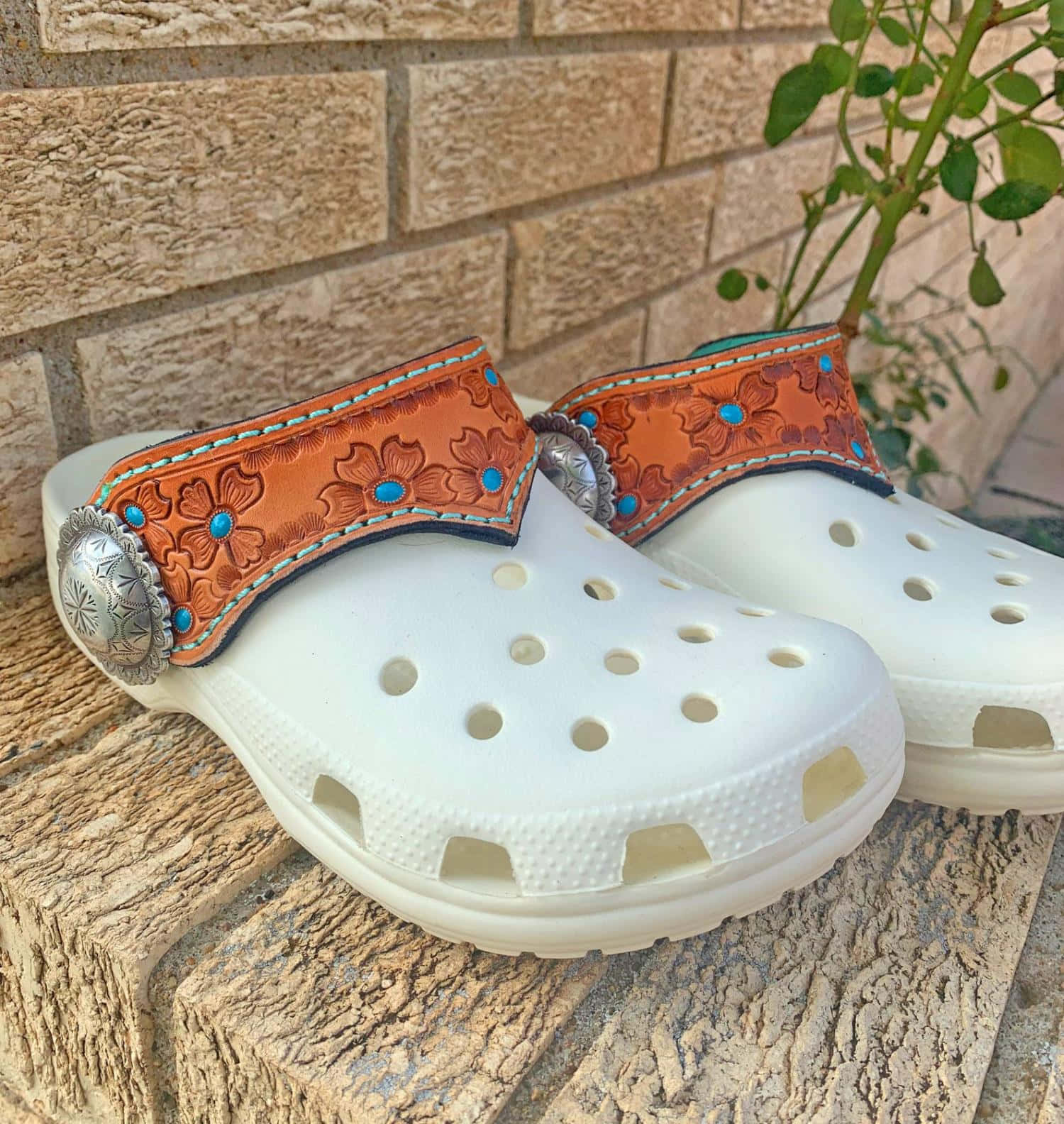 Crocs 桌布 壁紙 — 白色Crocs鞋，飾有華麗的橙色皮帶，帶有綠松石和銀色扣環，放在石檯上，背景是磚牆。