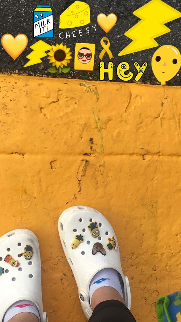 Crocs 桌布 壁紙 — 白色Crocs鞋搭配Minion吊飾，立於亮黃色牆壁旁，旁邊是覆蓋著俏皮黃色貼紙的黑色表面。
