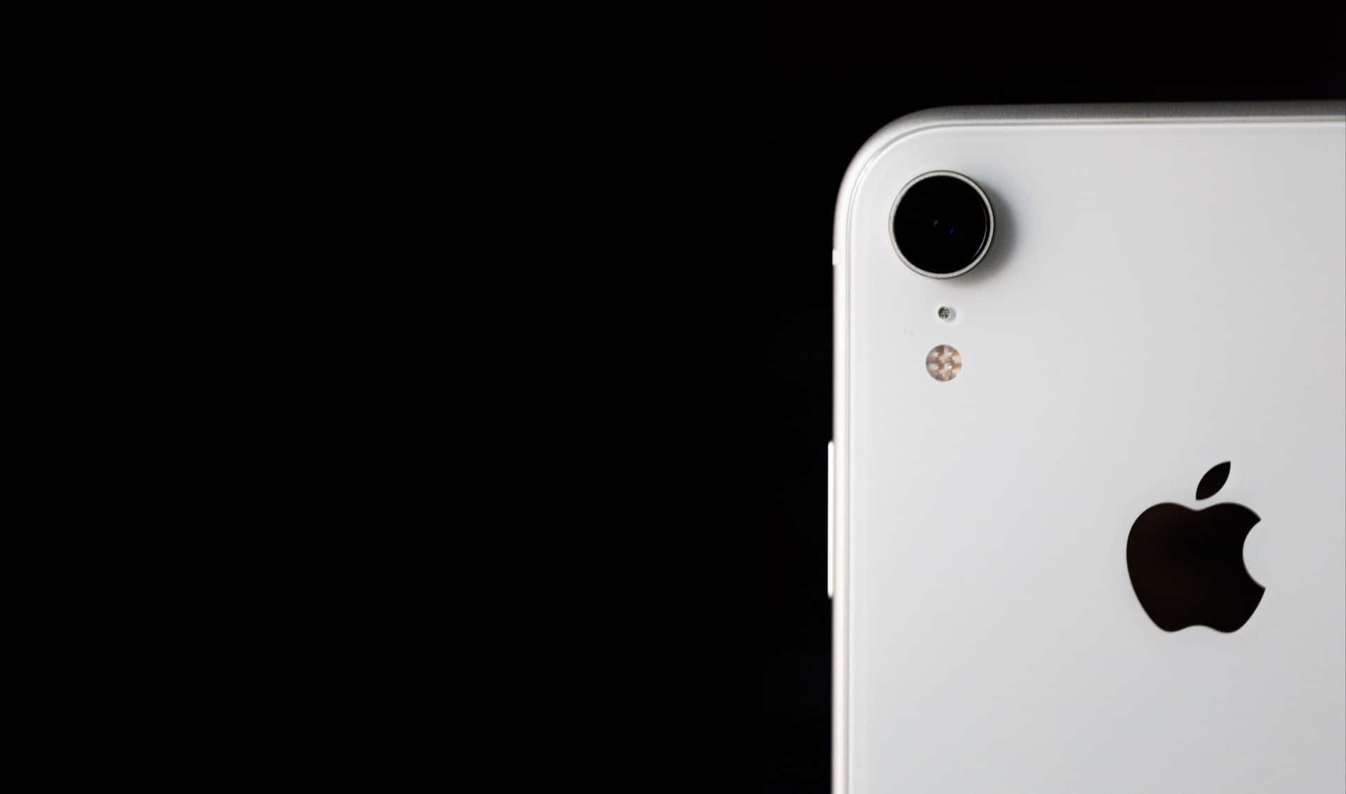  壁紙 — 白色iPhone XR背面角落的特寫，在純黑背景下突出其相機和Apple標誌。