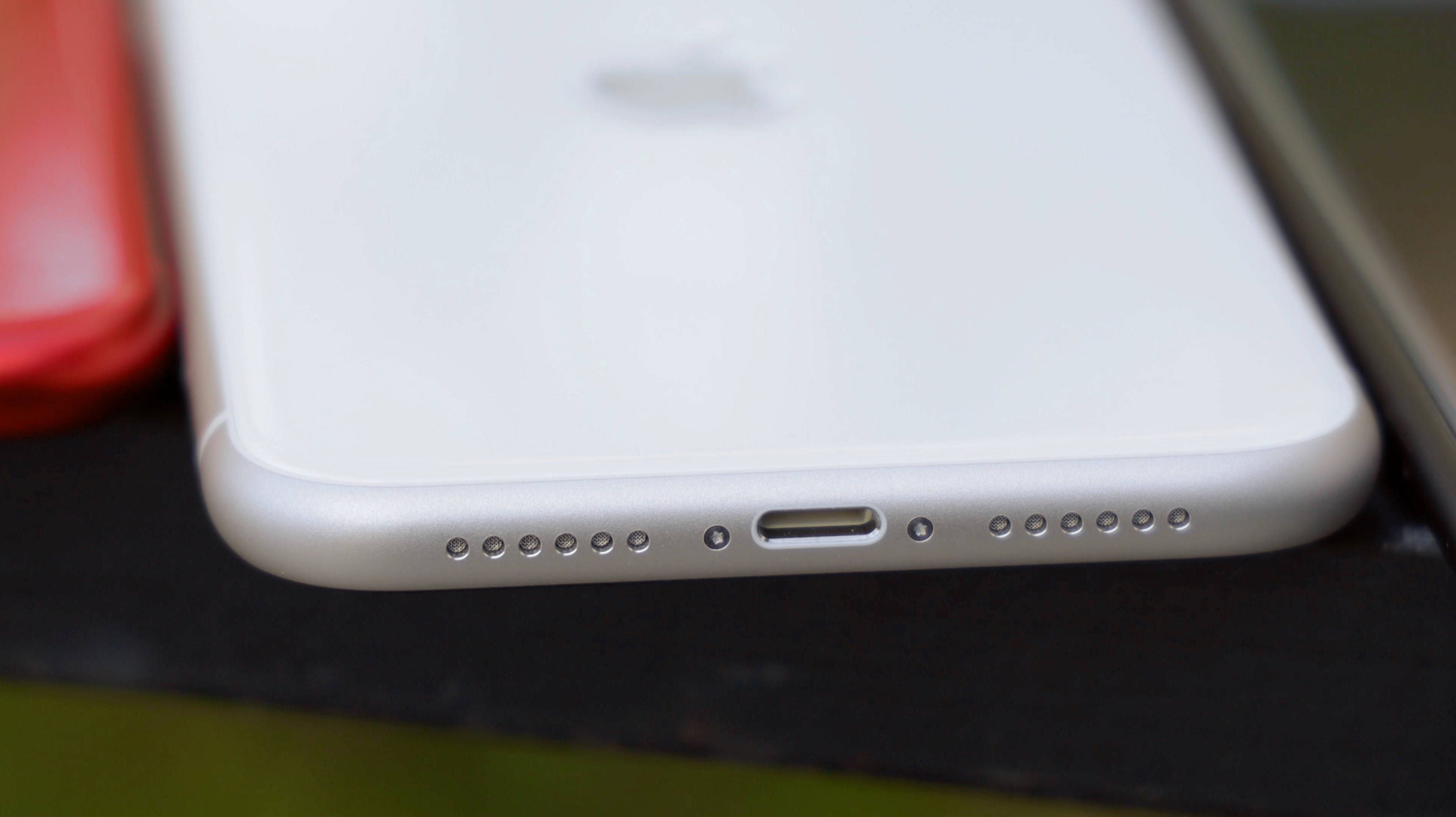 iPhone 11 桌布 壁紙 — 白色iPhone底部邊緣的特寫，顯示充電端口和揚聲器格柵，置於深色表面上。