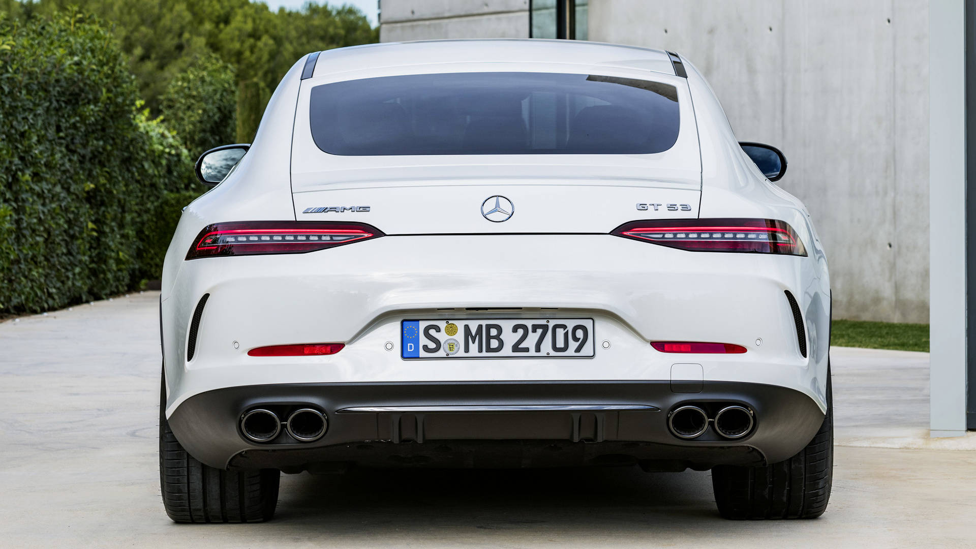 Mercedes Amg 桌布 壁紙 — 白色Mercedes-AMG GT S的後視圖，停放在混凝土車道上，旁邊有綠色樹籬和現代建築。