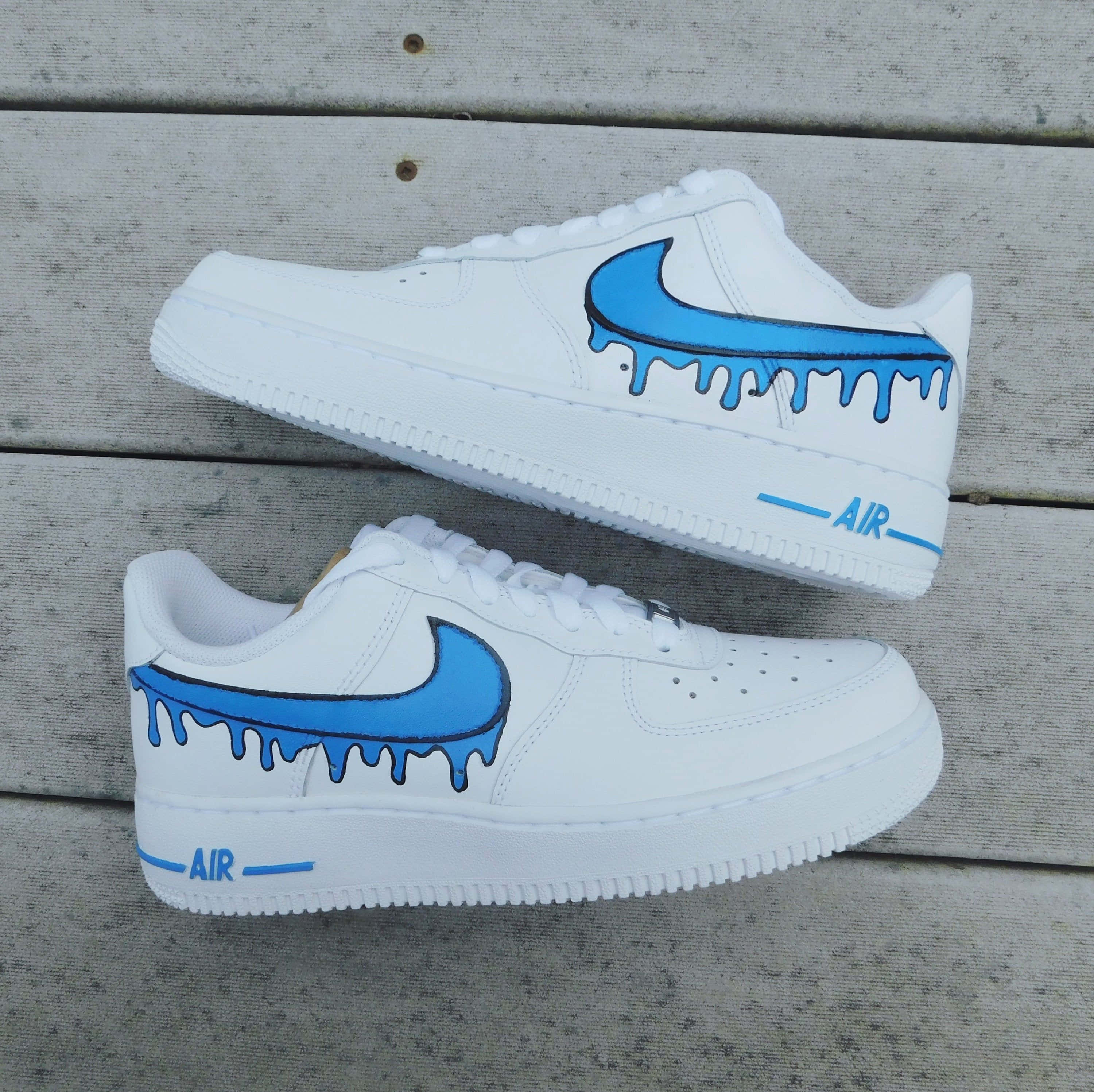 Nike Air Force 桌布 壁紙 — 白色Nike Air Force 1運動鞋帶有藍色滴落Swoosh，放在風化的木板上。
