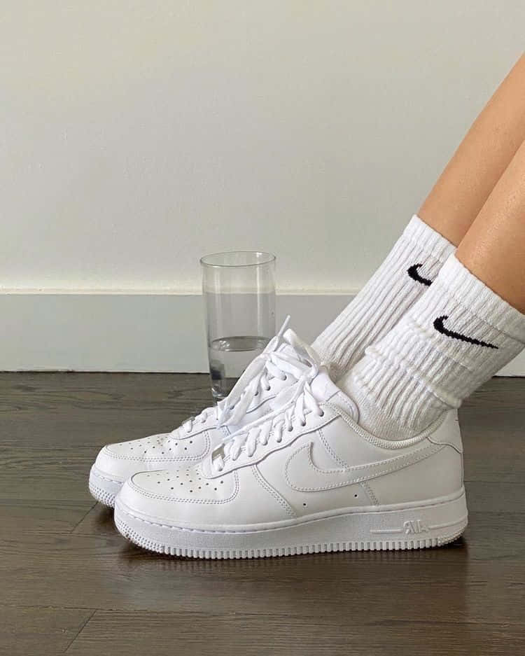 Nike Air Force 桌布 壁紙 — 白色Nike Air Force 1運動鞋和搭配的襪子放在木地板上，旁邊有一杯水。