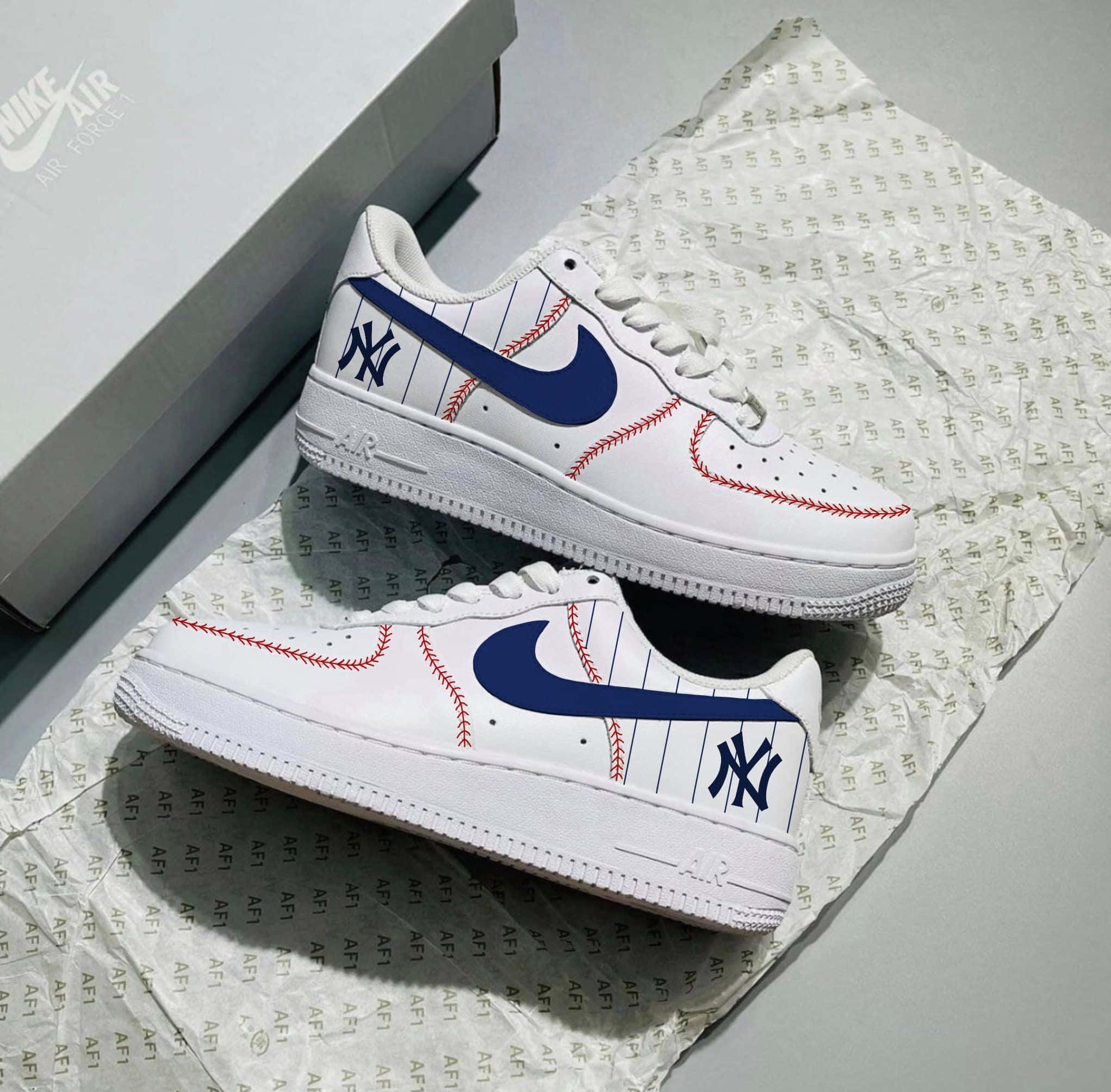 Nike Air Force 桌布 壁紙 — 白色Nike Air Force 1運動鞋，帶有藍色NY標誌和紅色棒球縫線，放在品牌紙巾上，旁邊有一個鞋盒。