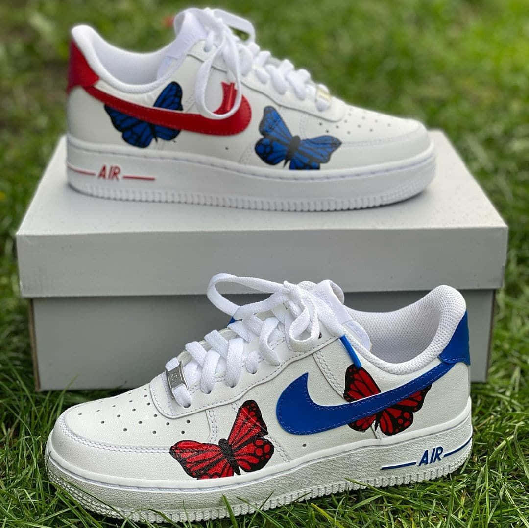 Nike Air Force 桌布 壁紙 — 白色Nike Air Force 1運動鞋，飾有紅色和藍色蝴蝶，放在綠色草地上的盒子上。