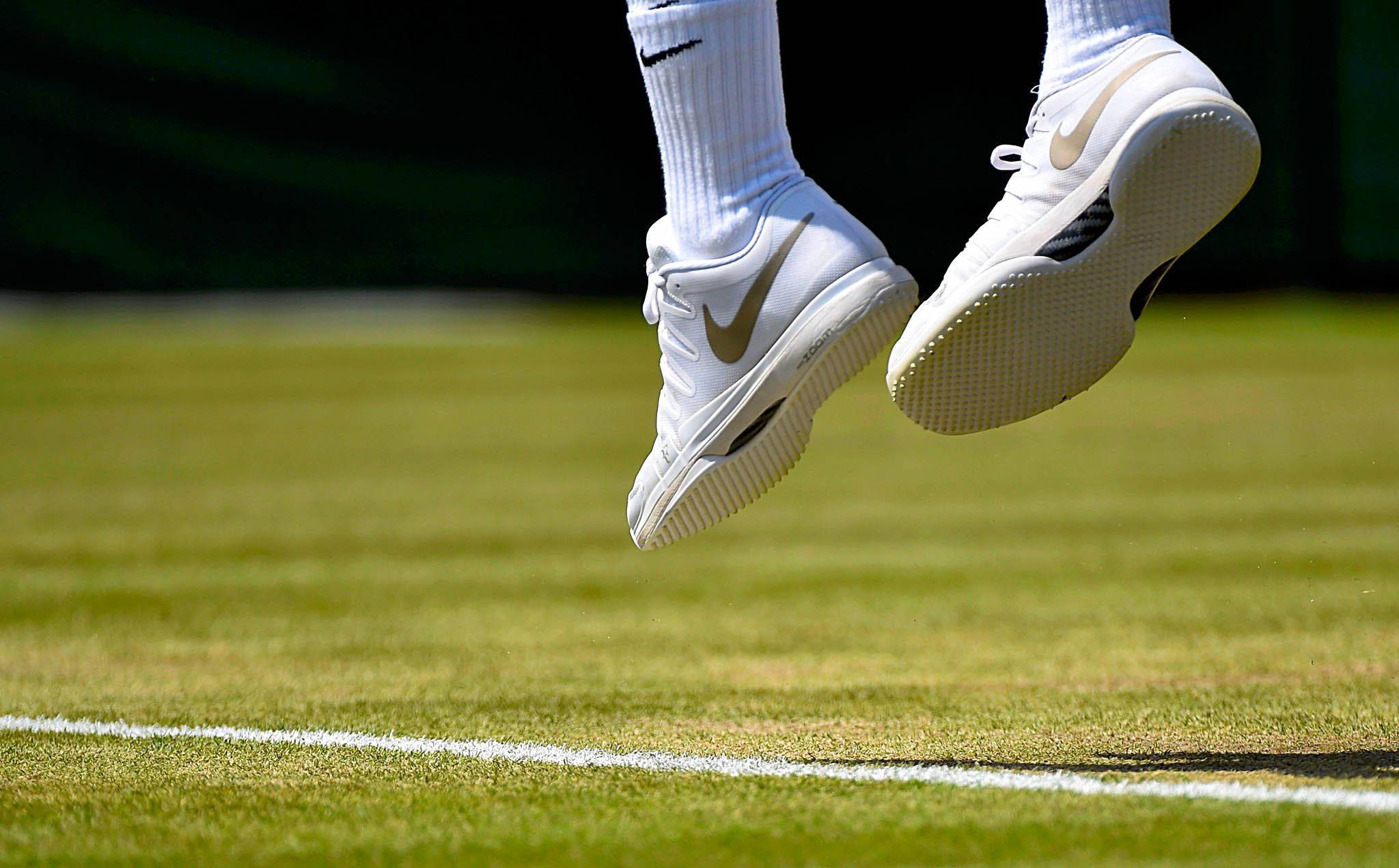 Wimbledon 桌布 壁紙 — 白色Nike網球鞋在綠色草地場地上方半空中的特寫，帶有清晰的白色線條。