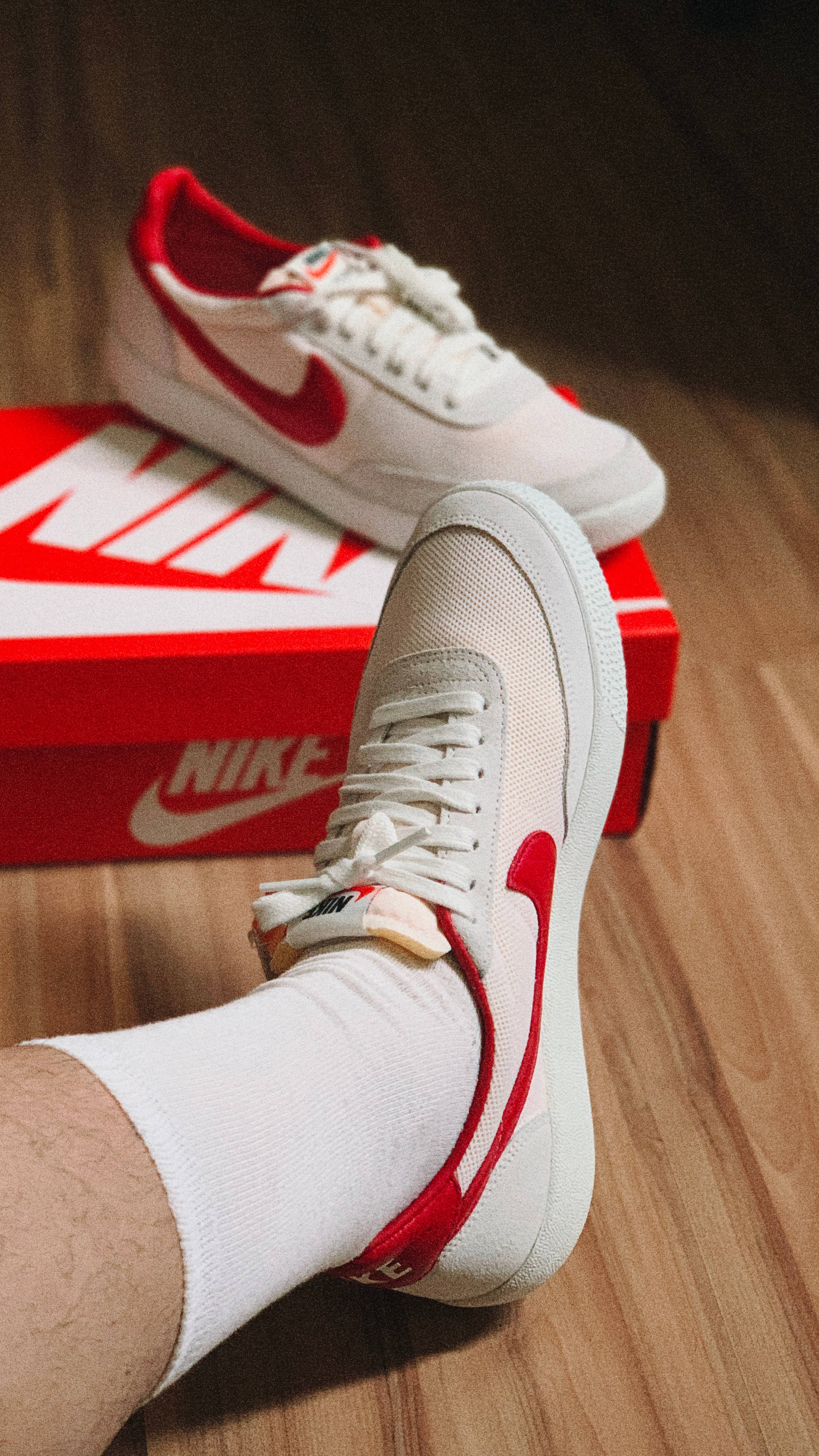 Nike iPhone 桌布 壁紙 — 白色Nike運動鞋帶紅色勾勾，放在木地板上的紅色盒子上，搭配白色襪子穿著。