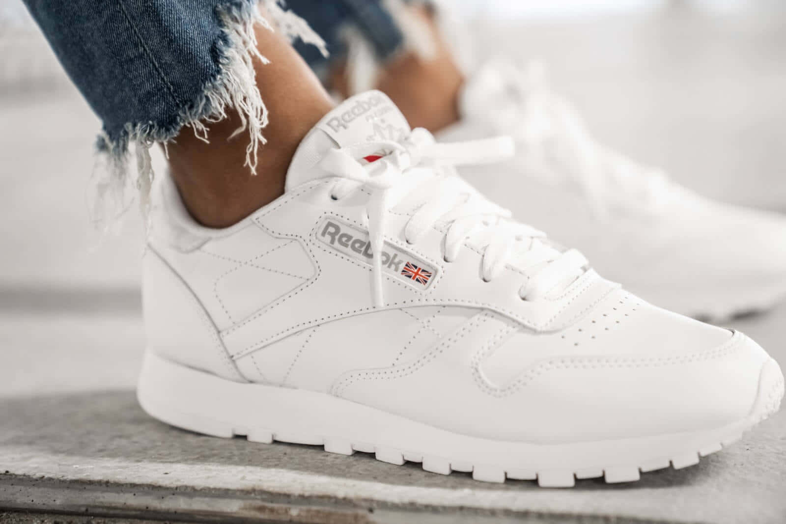 Reebok 桌布 壁紙 — 白色Reebok運動鞋搭配磨邊牛仔褲在混凝土表面上的特寫。