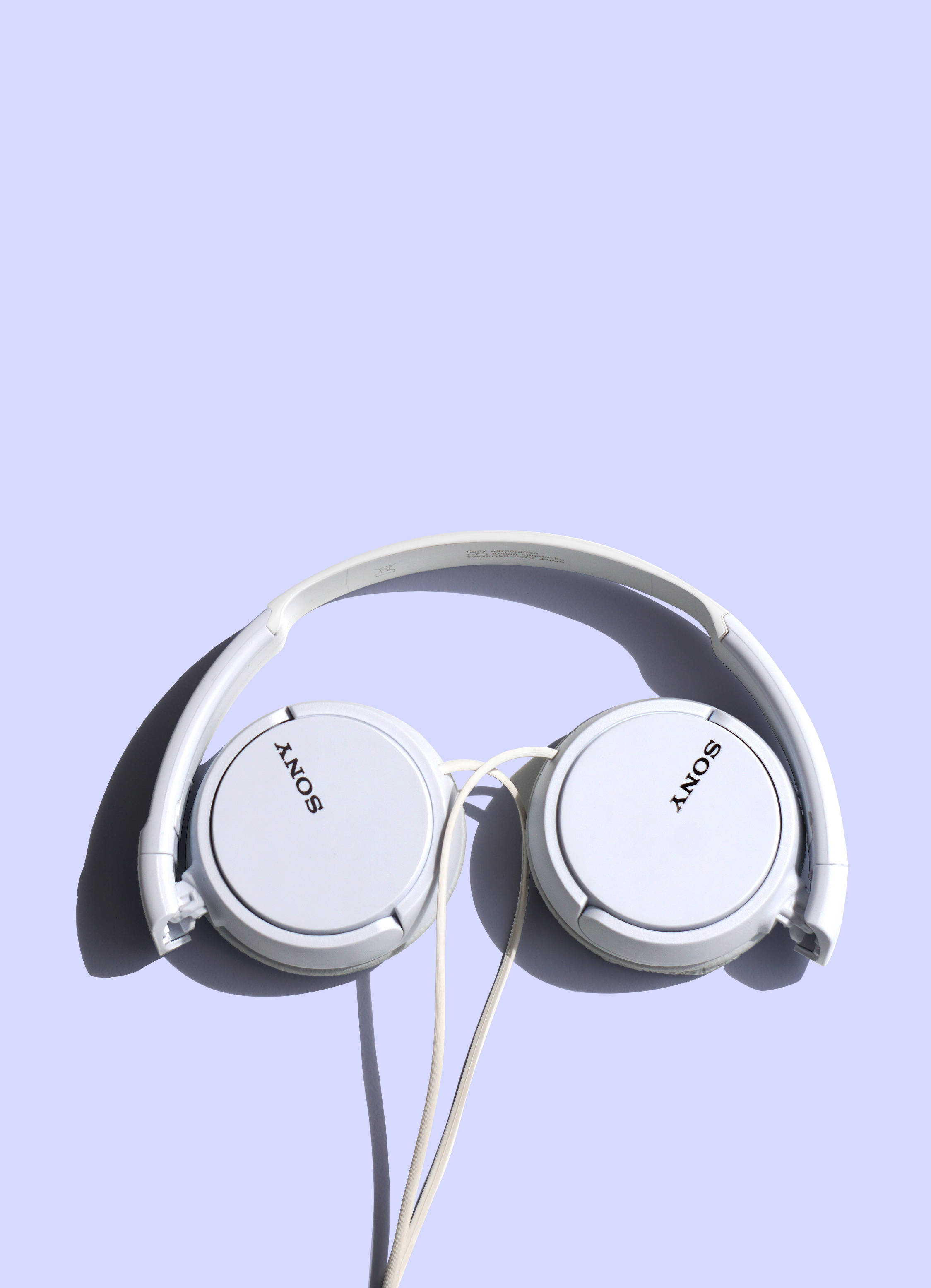 Sony 桌布 壁紙 — 白色Sony耳罩式耳機在簡約的攝影棚燈光下，於純色薰衣草背景上投下柔和陰影。