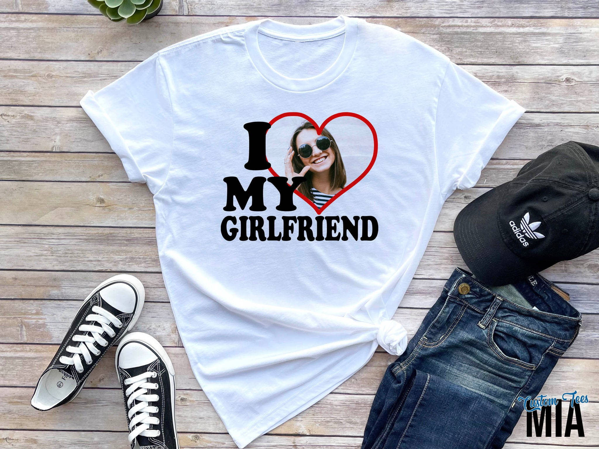 I Love My Girlfriend 桌布 壁紙 — 白色T恤，上面有心形圖案中微笑女性的照片，周圍是牛仔褲、運動鞋和帽子，放在木地板上。