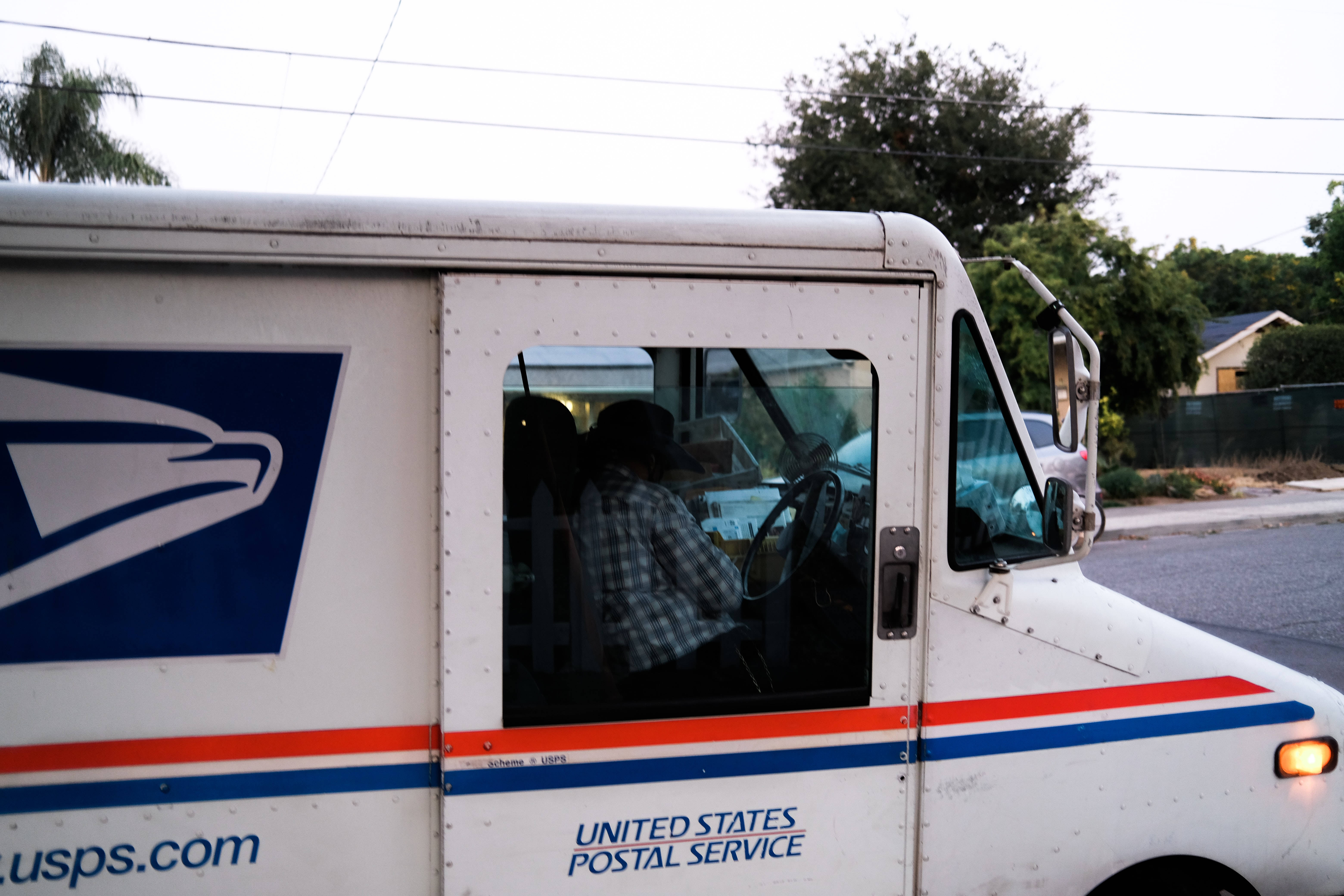 Person 桌布 壁紙 — 白色USPS送貨車的特寫，透過車窗可見司機穿著格子襯衫。