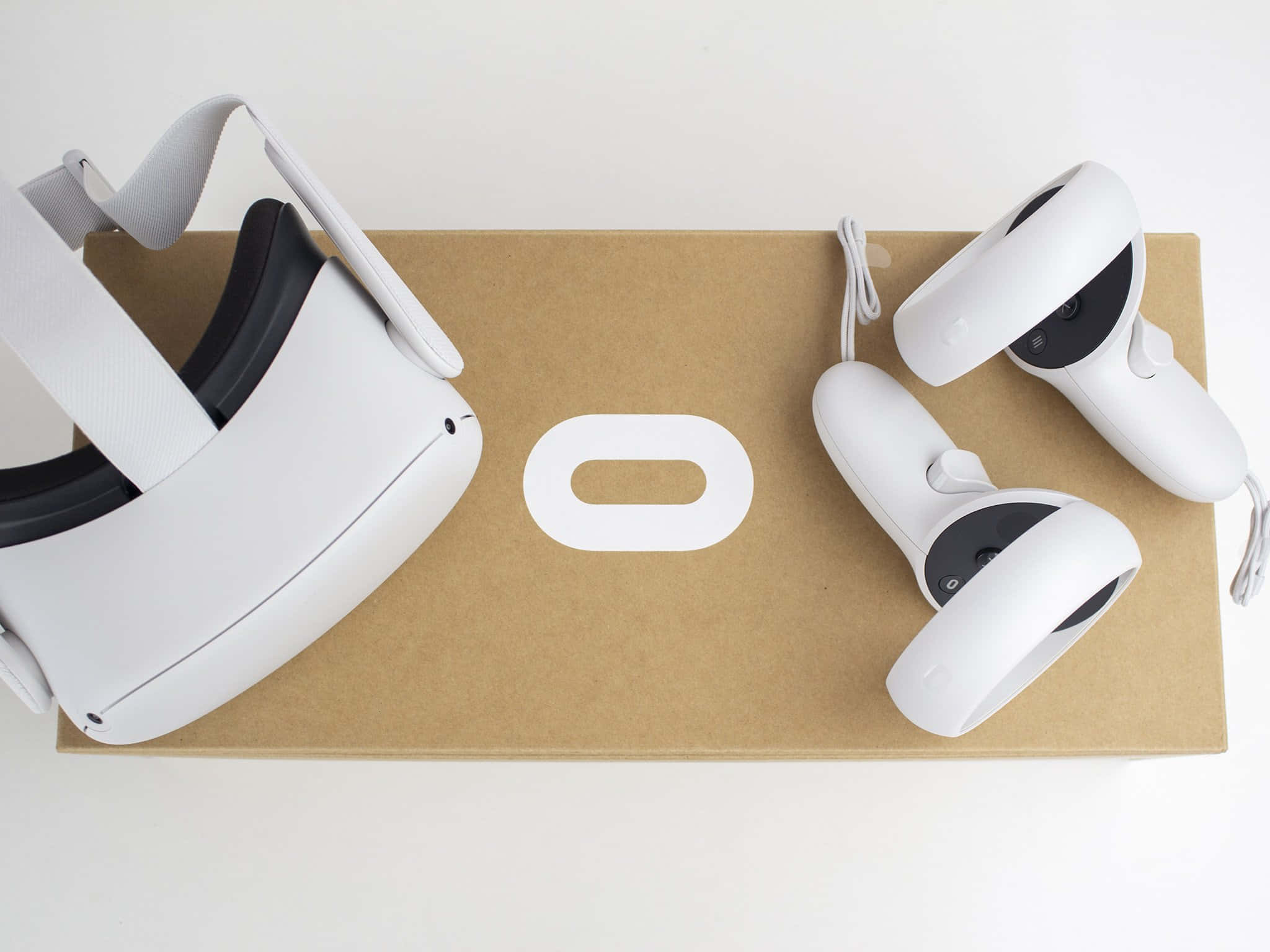 Oculus Quest 2 桌布 壁紙 — 白色VR頭戴式裝置和控制器整齊地放在一個帶有極簡標誌的棕色紙箱上，背景是潔淨的白色。