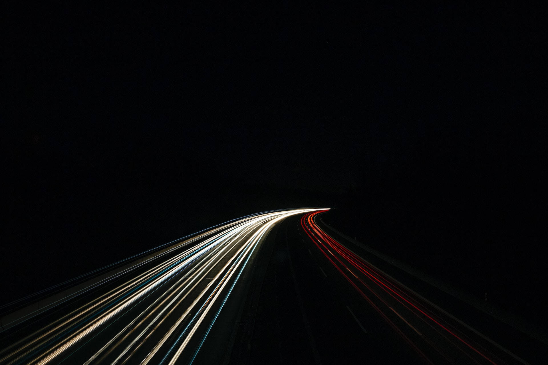 黑色 桌布 壁紙 — 白色和紅色車燈的條紋在夜晚黑暗蜿蜒的道路上模糊，營造出速度和動感。