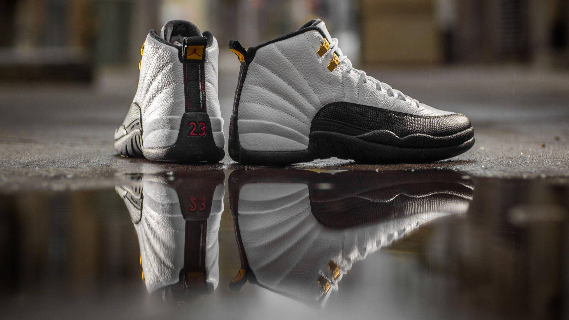 Jordan球鞋 桌布 壁紙 — 白色和黑色的Jordan 12運動鞋，紅色23，倒映在濕漉漉的人行道水坑中。