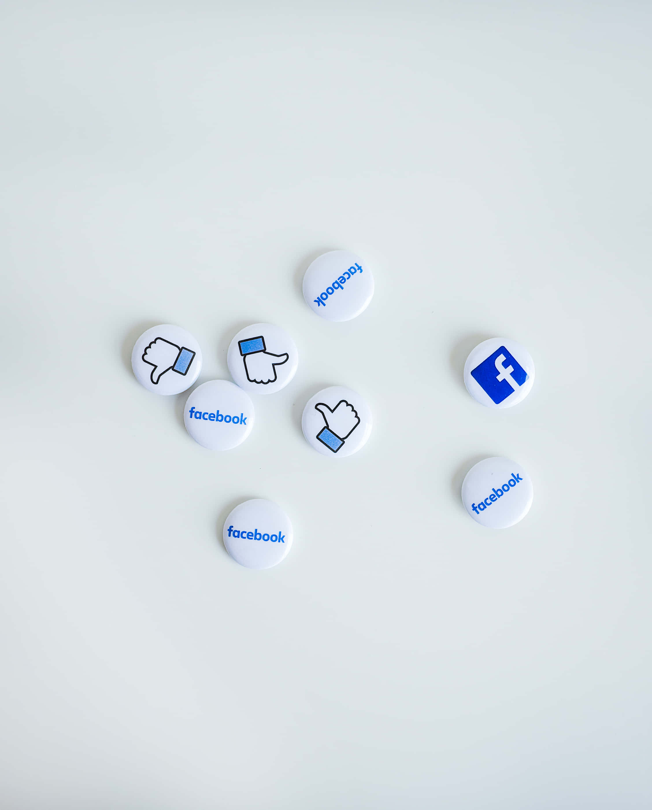 Facebook 桌布 壁紙 — 白色圓形Facebook主題按鈕，帶有豎起拇指和向下拇指及標誌，散落在純淺灰色表面上。