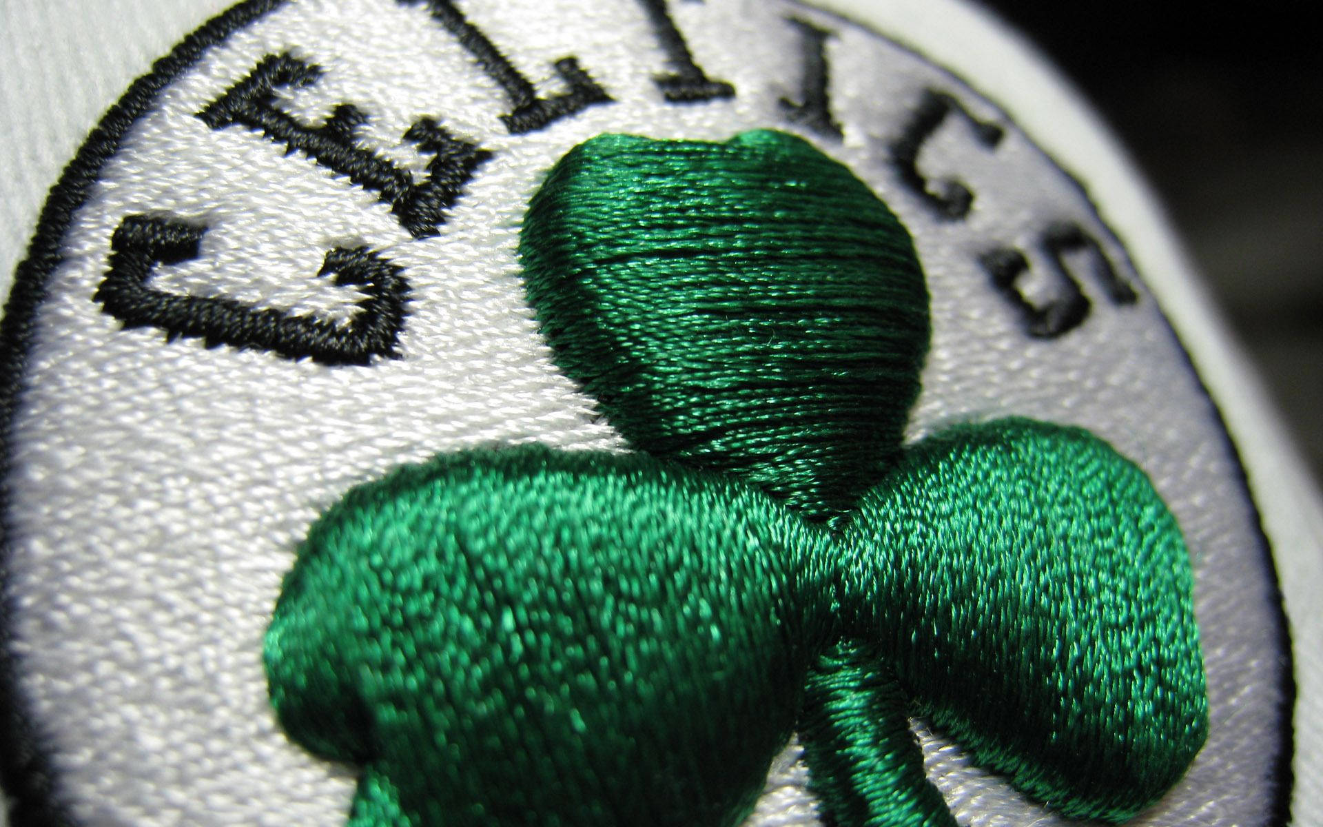 Celtics 桌布 壁紙 — 白色圓形布章上，精細的綠色刺繡三葉草和黑色 'CELTICS' 文字的近距離特寫。