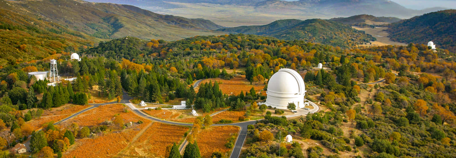 Observatory 桌布 壁紙 — 白色圓頂天文台坐落在秋日山丘中的鳥瞰圖，蜿蜒的道路和散落的樹木。