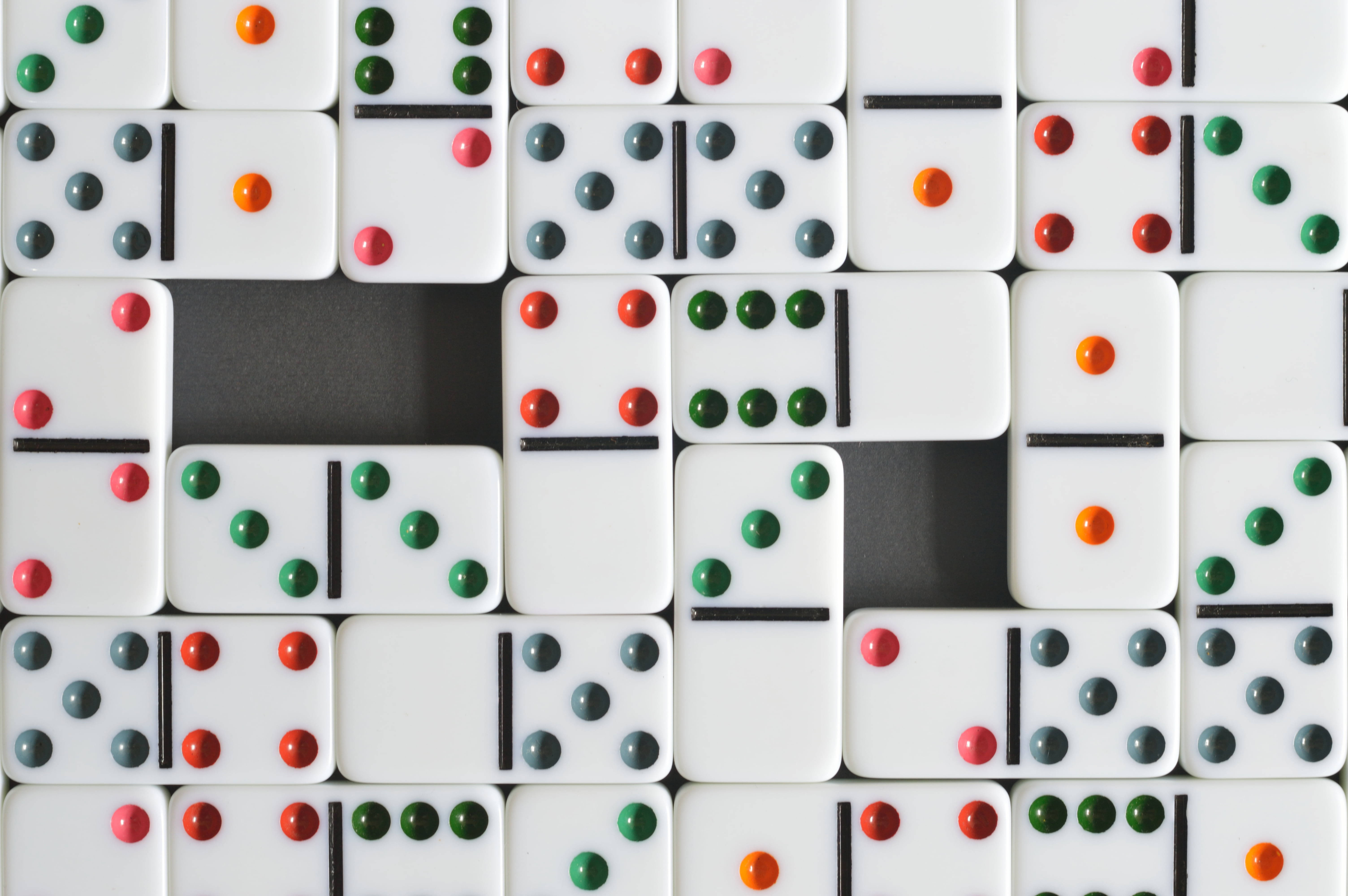 Domino 桌布 壁紙 — 白色多米諾骨牌帶有紅色、綠色和橙色圓點，在深色表面上以分散圖案排列。