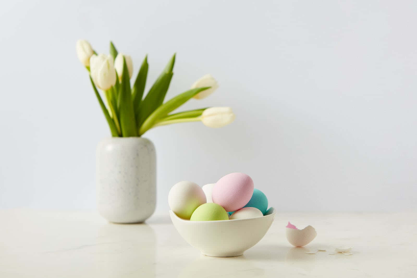 Pastel Easter 桌布 壁紙 — 白色大理石清潔表面上，白色鬱金香花瓶旁邊的白色碗中盛放著粉彩色的雞蛋。