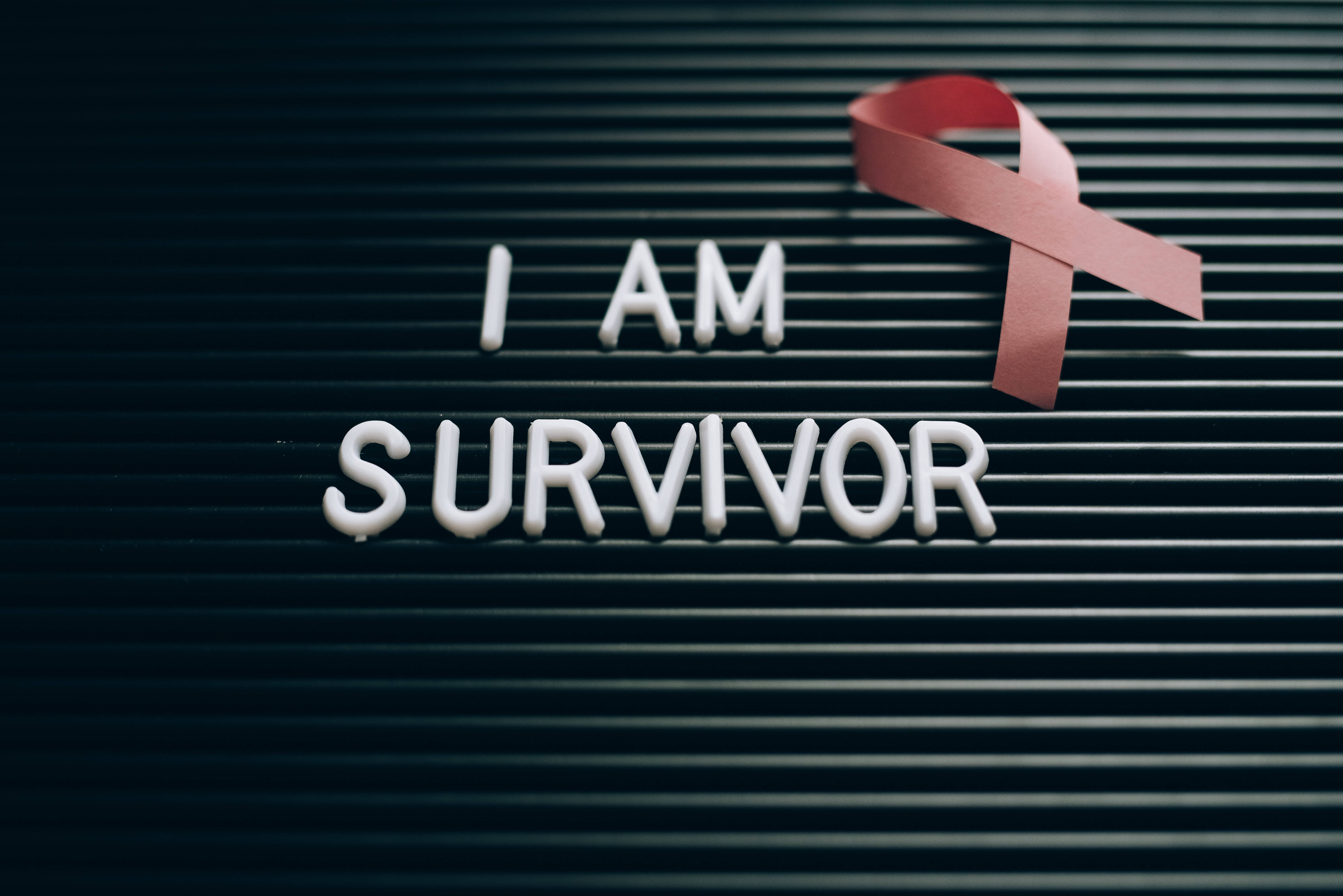 Breast Cancer Awareness 桌布 壁紙 — 白色字母在深色板條板上拼出 I AM SURVIVOR，旁邊有一個紅色意識絲帶。