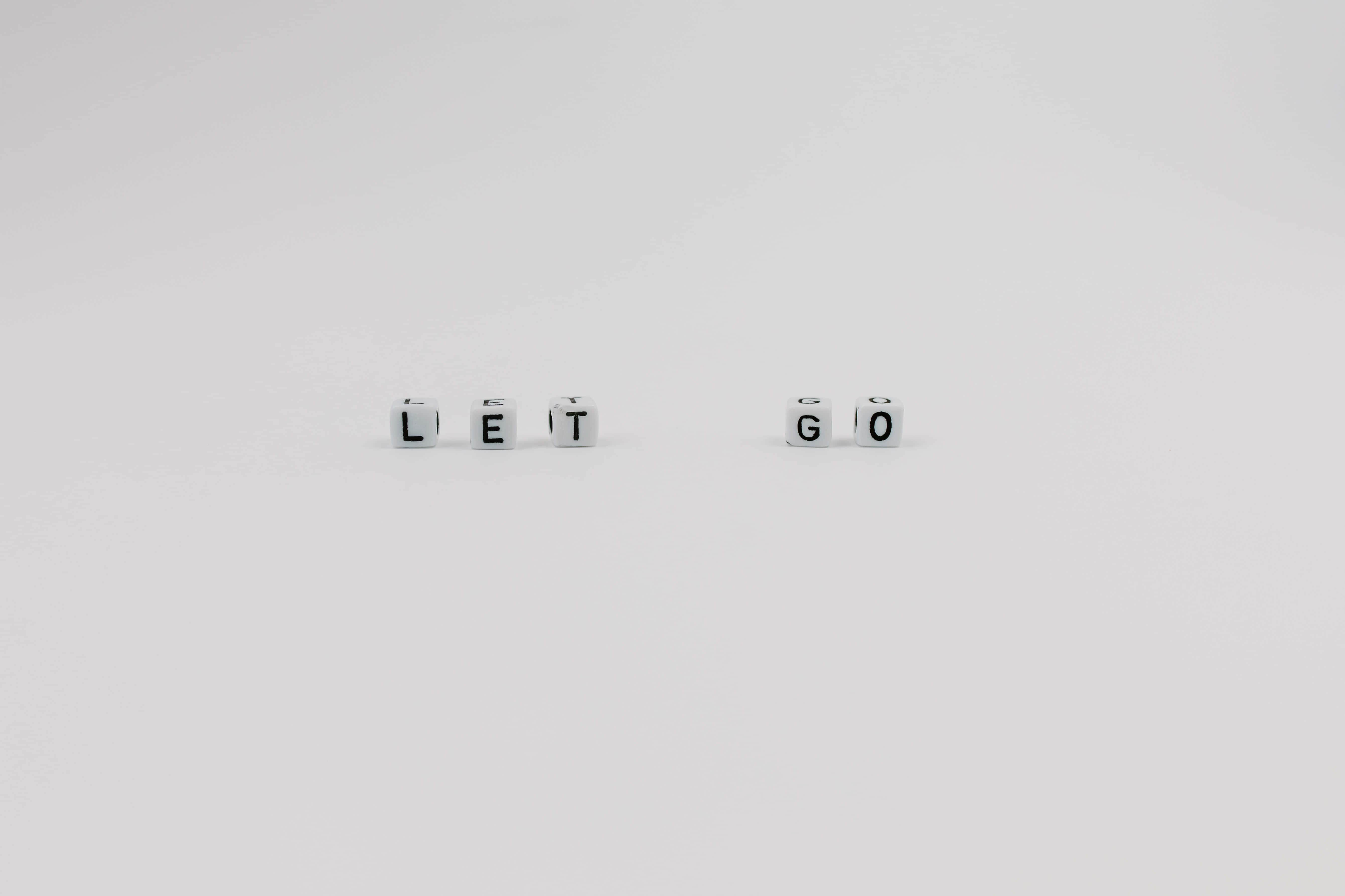語錄 桌布 壁紙 — 白色字母方塊拼出 LET GO，間隔放置在純白表面上。
