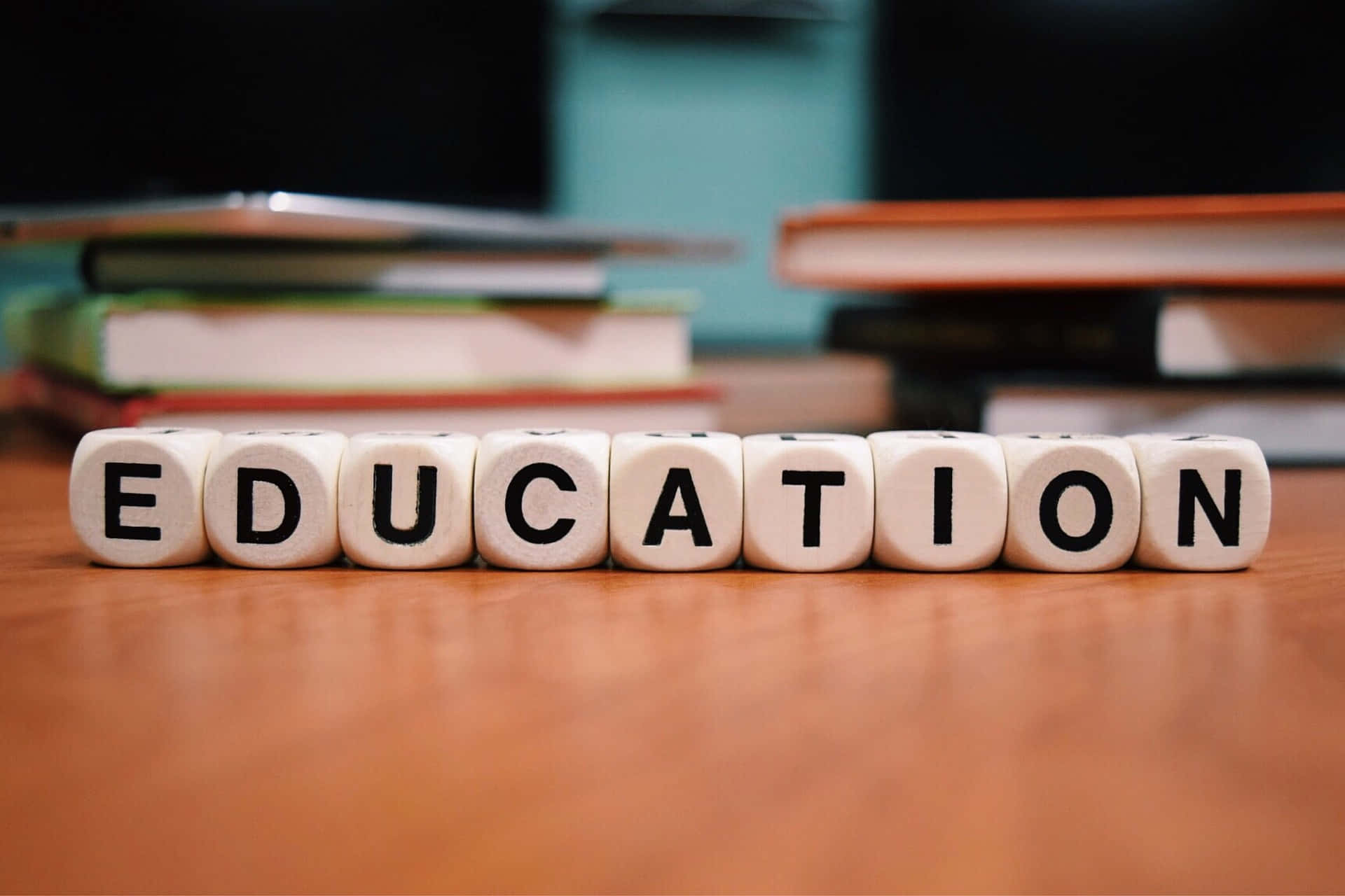Education 桌布 壁紙 — 白色字母方塊拼出教育一詞，放在木桌上，後面有模糊的書堆。