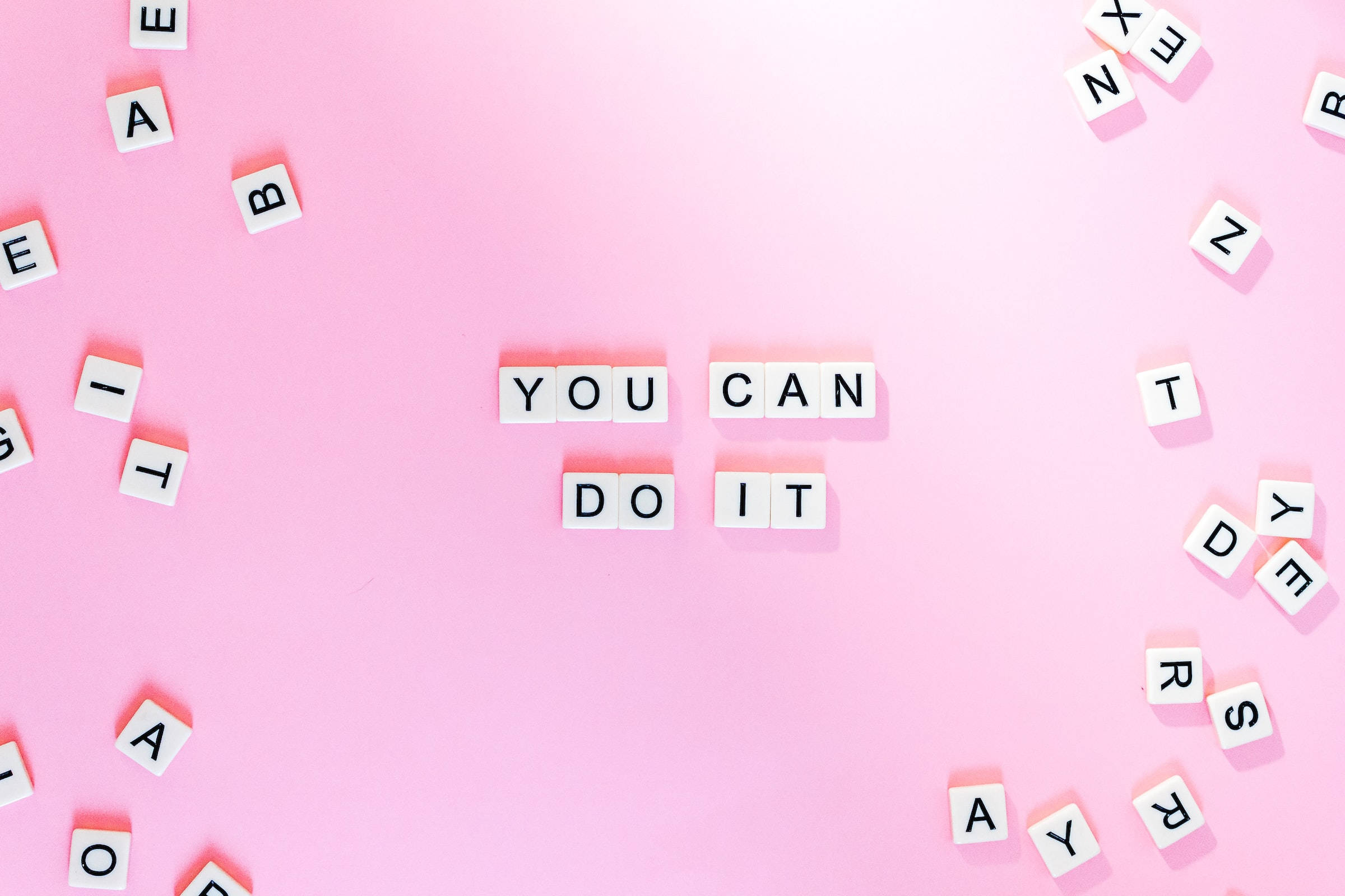 you can do it 桌布 壁紙 — 白色字母瓷磚在柔和的粉紅色背景中央拼出 'YOU CAN DO IT'，周圍散落著字母。