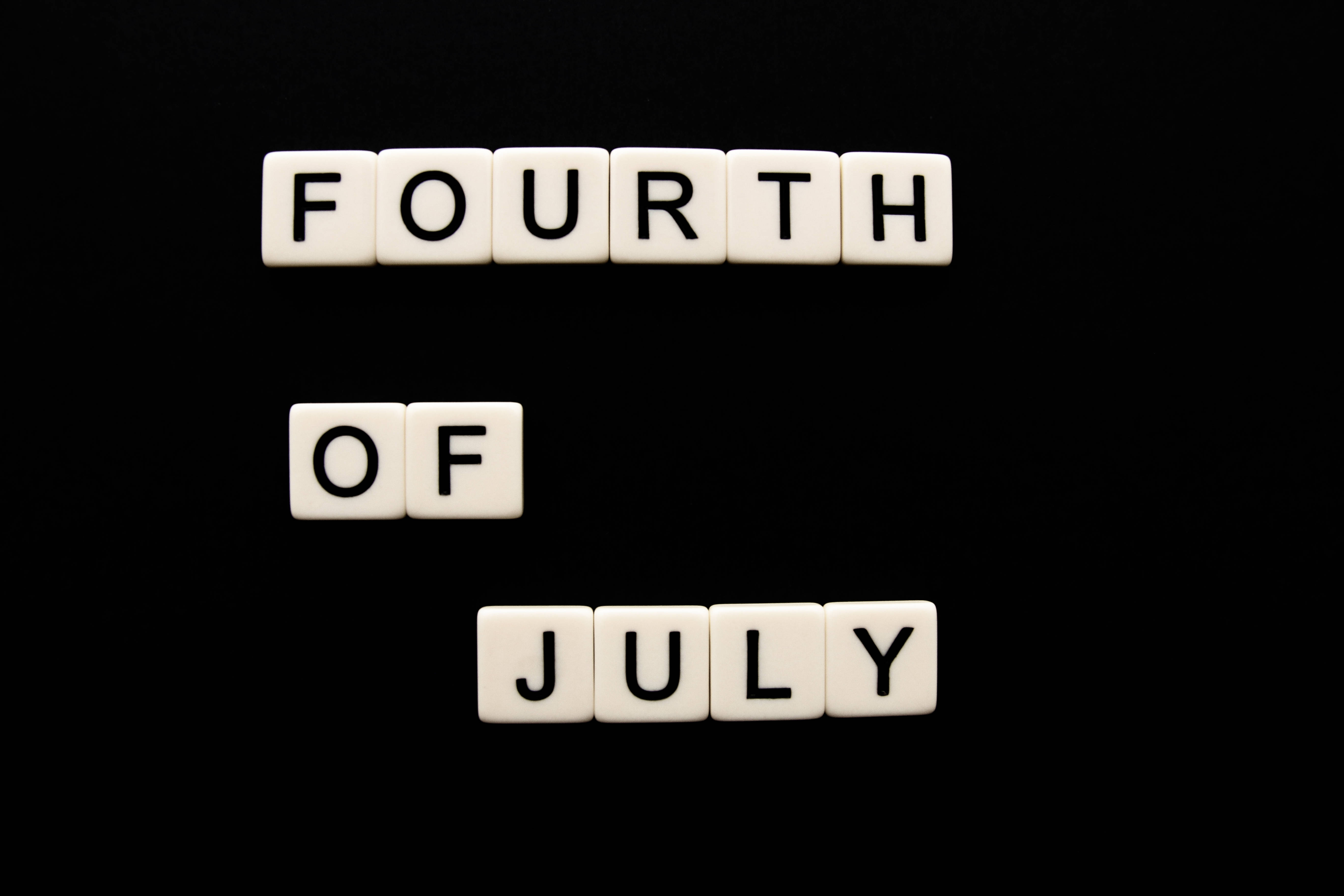 七月 桌布 壁紙 — 白色字母瓷磚拼出 fourth of july，垂直排列在純黑色背景上。