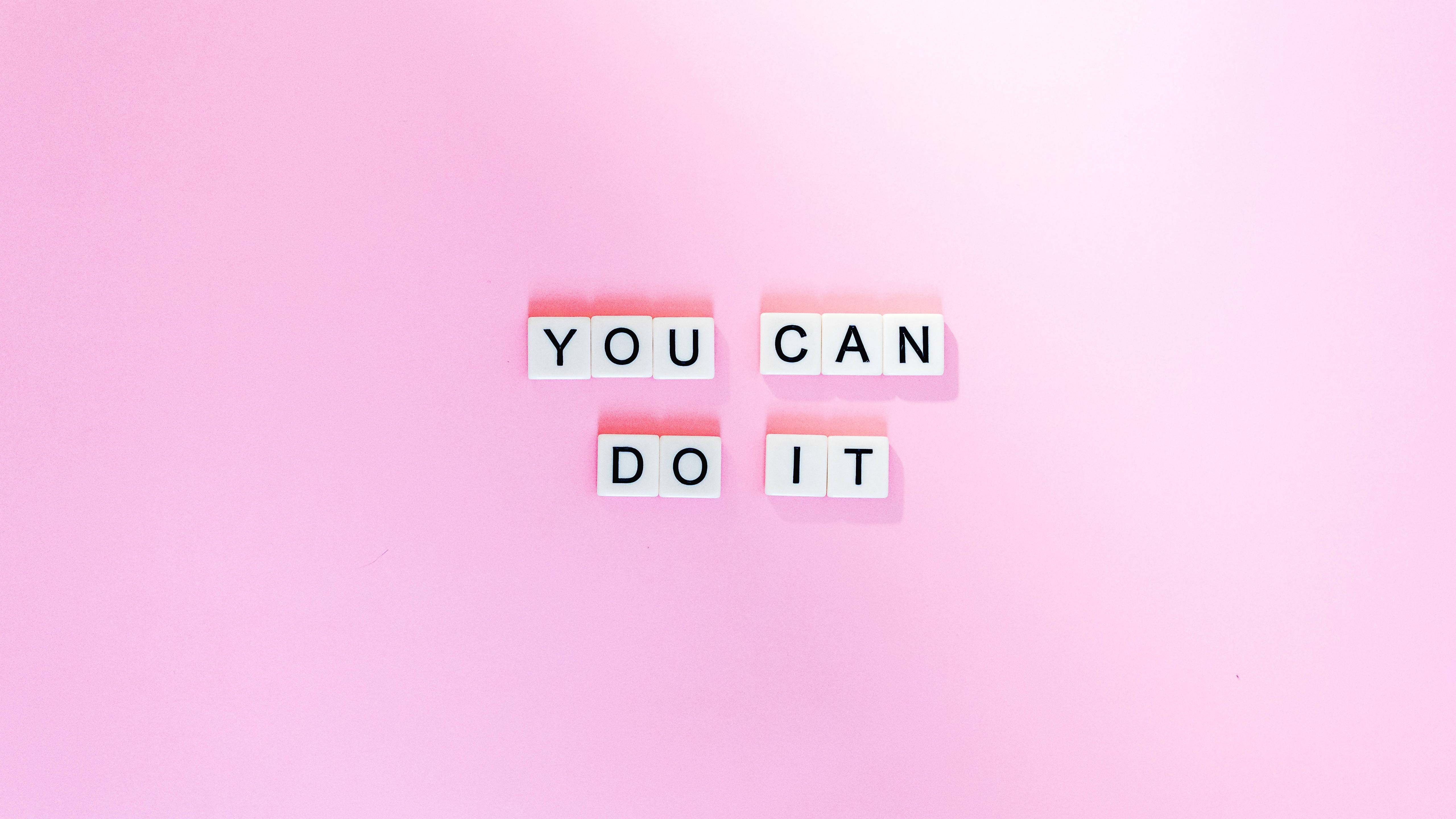 粉紅色 桌布 壁紙 — 白色字母瓷磚拼出「YOU CAN DO IT」，排列在柔和的粉紅色背景上，帶有微妙的陰影。