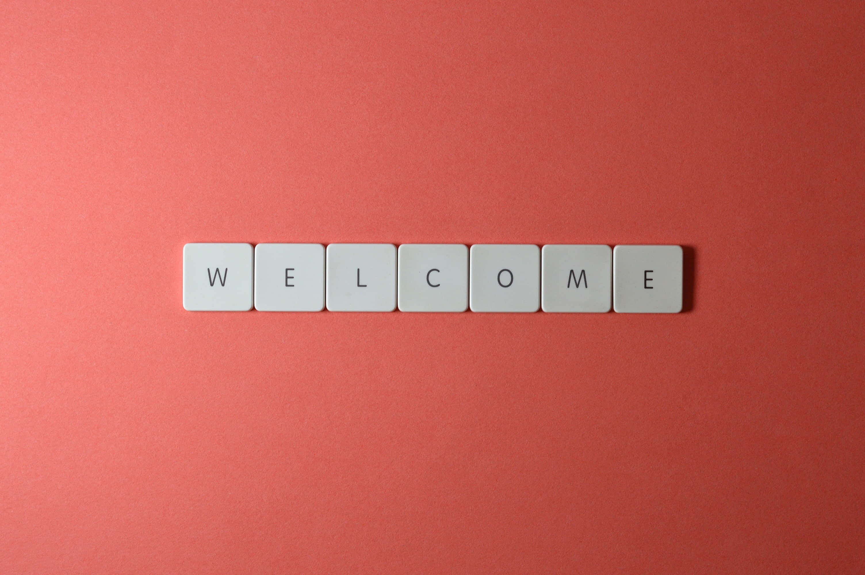 Welcome 桌布 壁紙 — 白色字母瓷磚拼出歡迎，居中放置在純珊瑚粉紅色背景上。