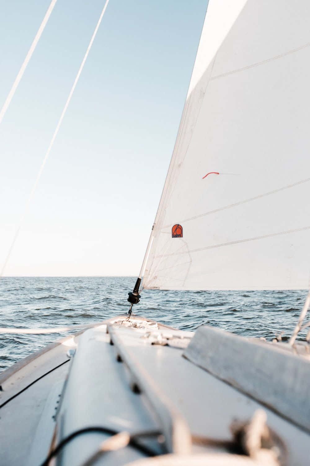 Sailboat 桌布 壁紙 — 白色帆船在晴朗天空下，從船頭視角在平靜的藍色海面上滑行。