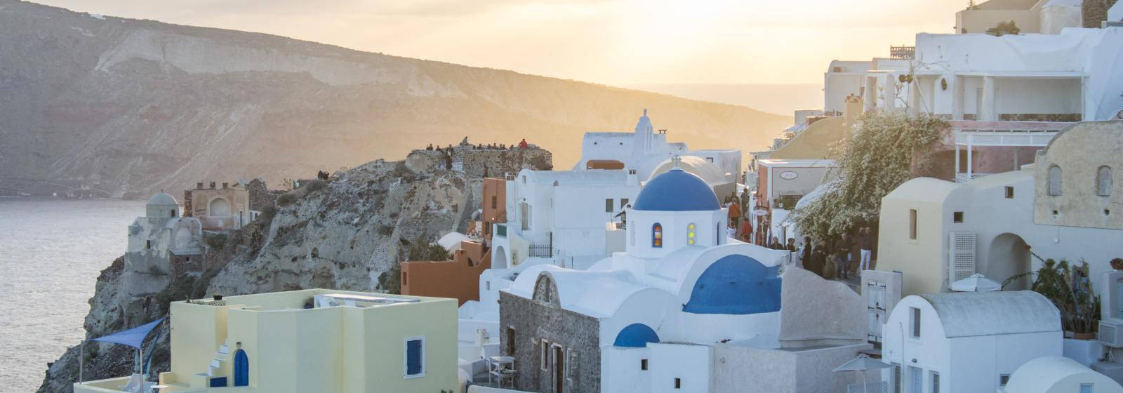 Santorini 桌布 壁紙 — 白色建築物與藍色圓頂依附在懸崖上，俯瞰金色日落時分的大海。