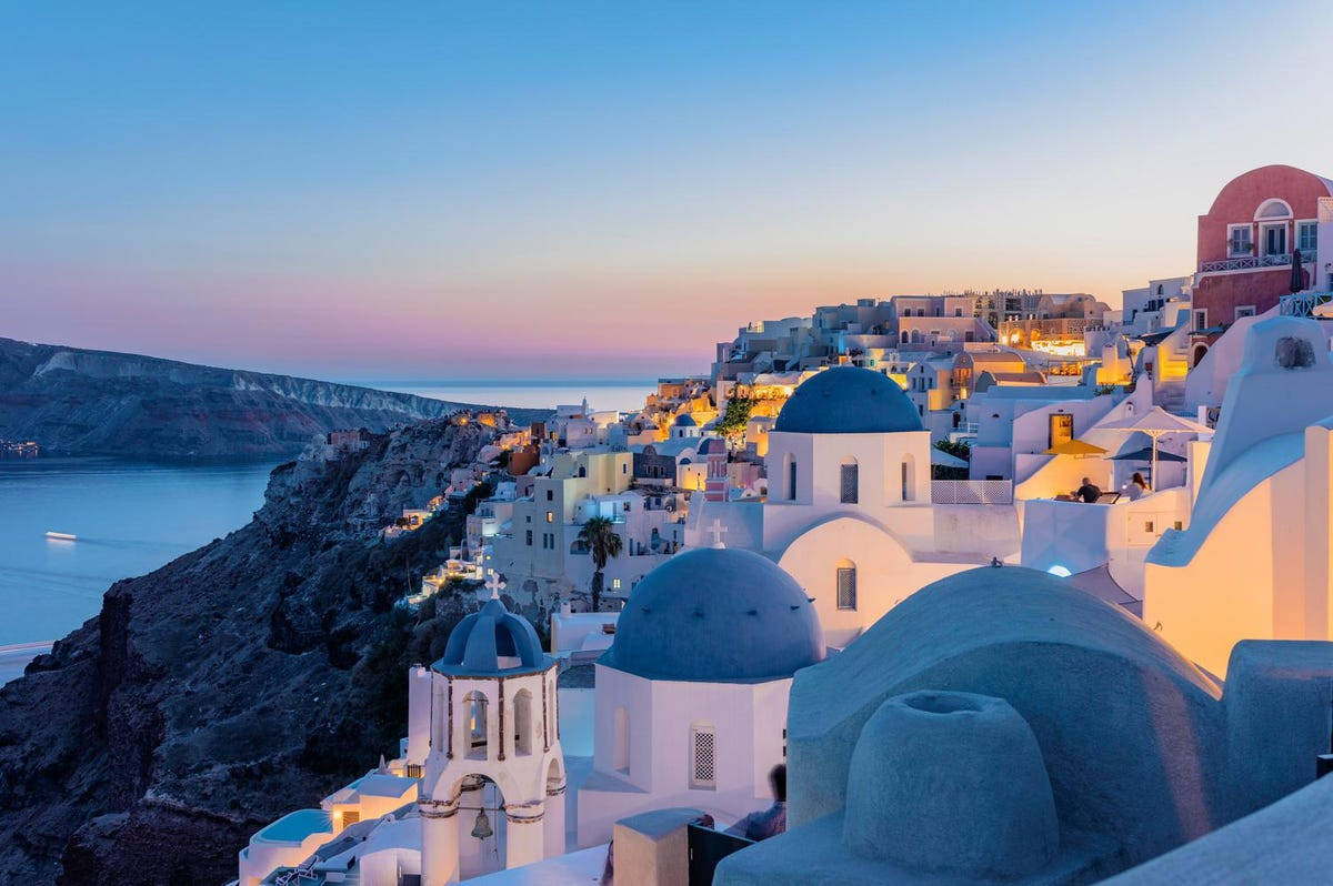Santorini 桌布 壁紙 — 白色建築物與藍色圓頂在黃昏時依附在懸崖邊，俯瞰平靜的大海。